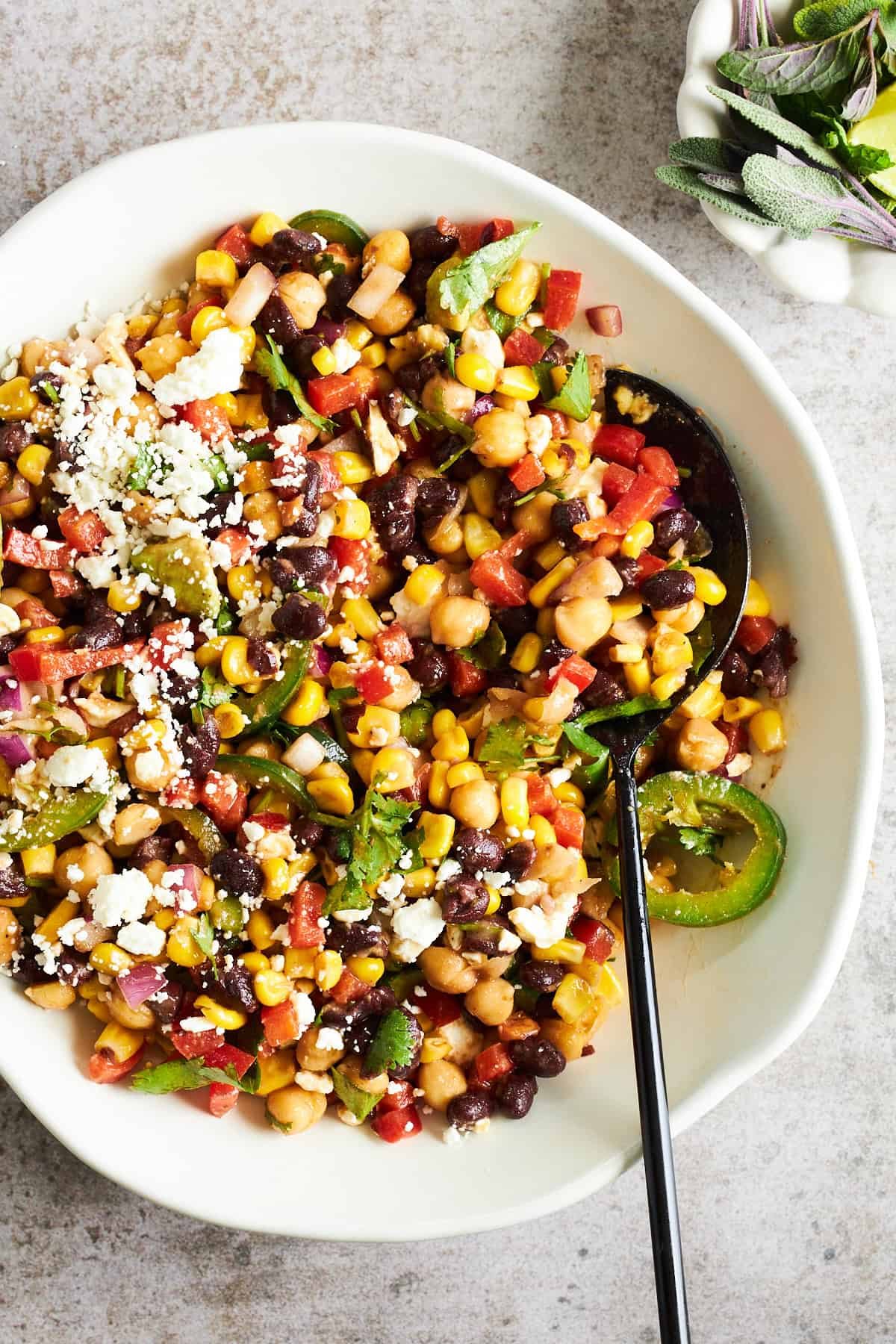 A bowl of Black Bean and Corn Salad with Sweet and Spicy Dressing with a spoon sticking out.