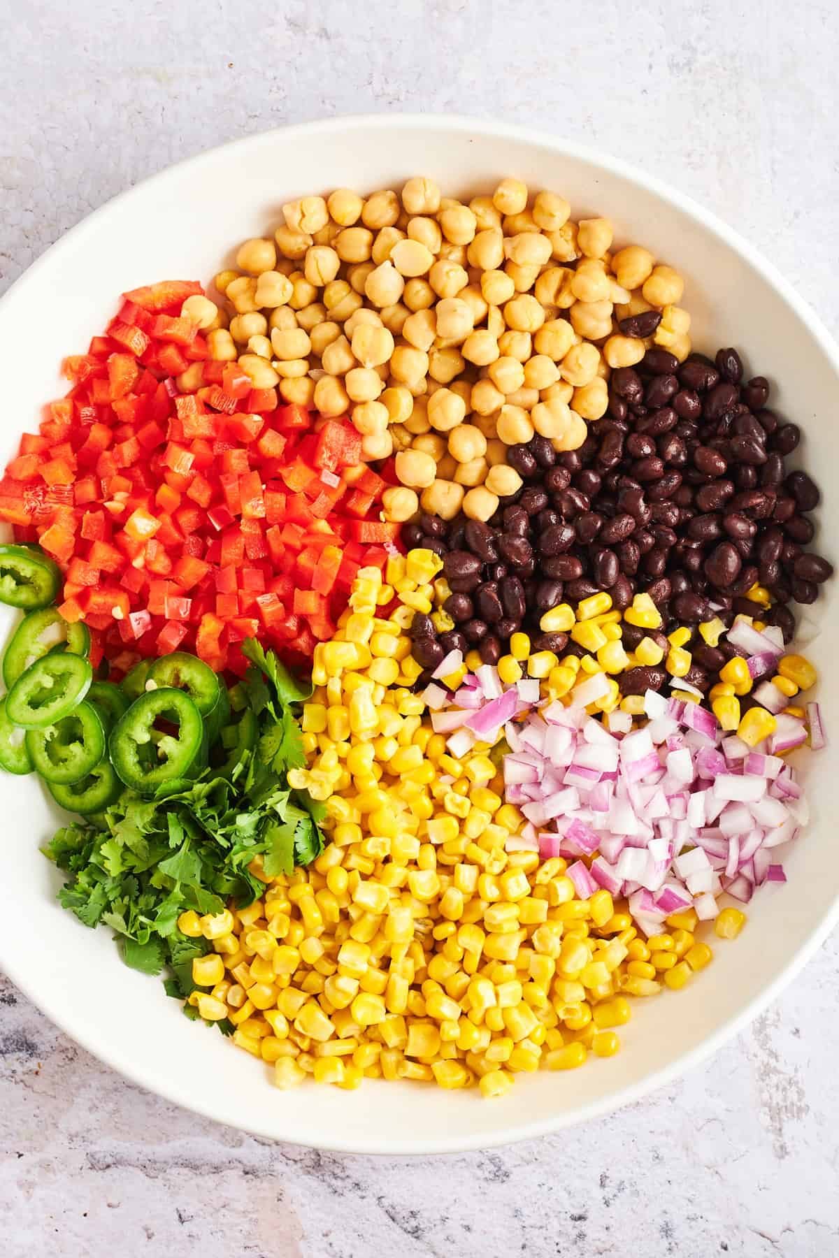 A bowl of diced red pepper, chickpeas, black beans, red onion, corn, cilantro, and jalapeño.