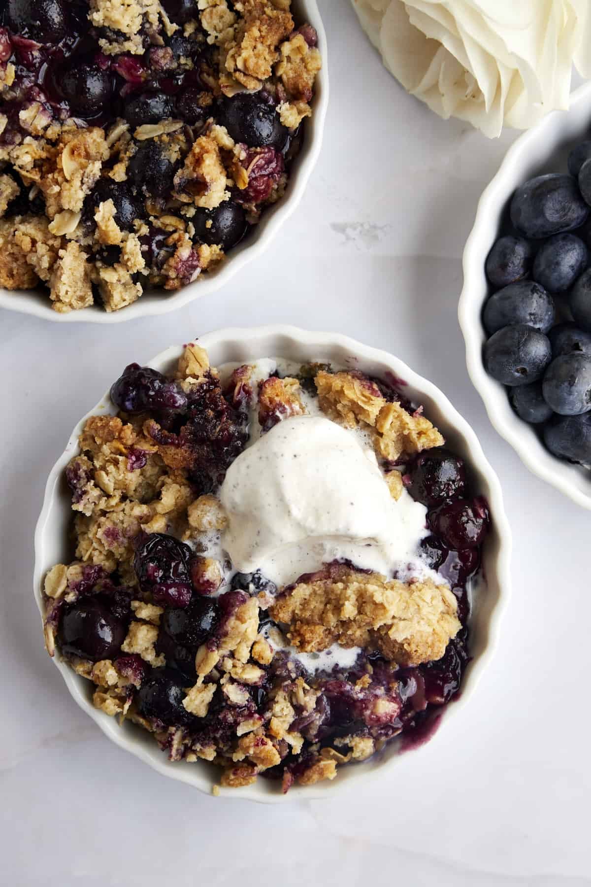 Overhead image of a ramekin full of blueberry crisp with melting vanilla ice cream on top.