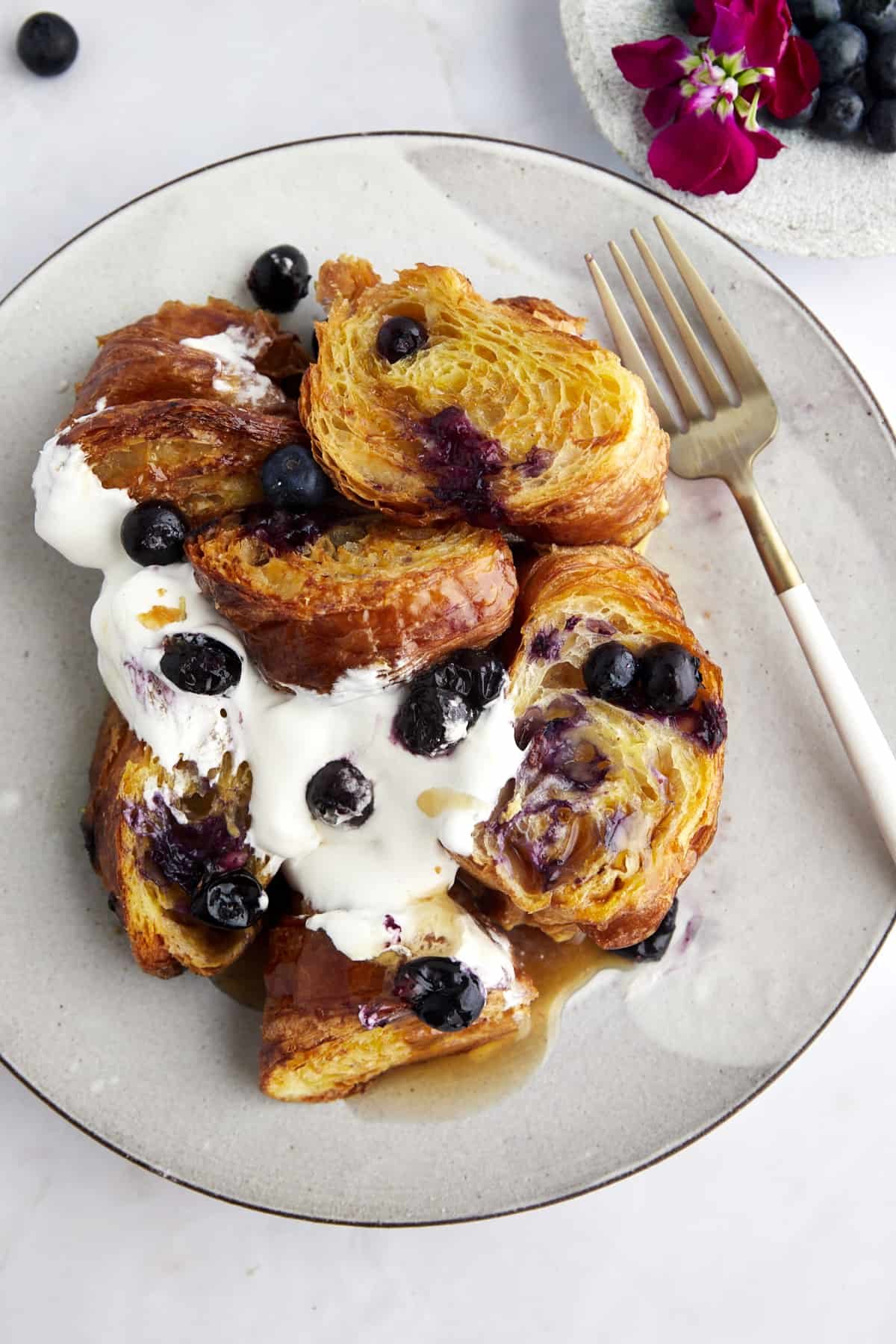 A plate of croissant blueberry French toast topped with yogurt, blueberries, and syrup.