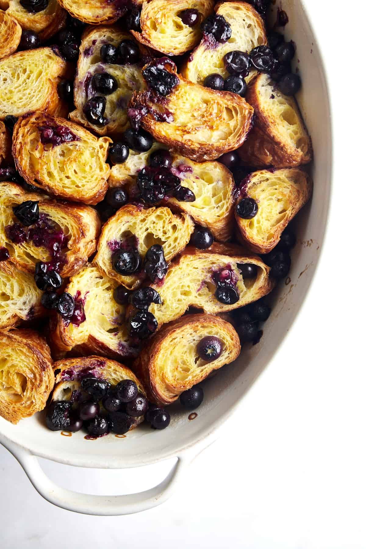 Overhead image of croissant pieces in a baking dish with blueberries on top.