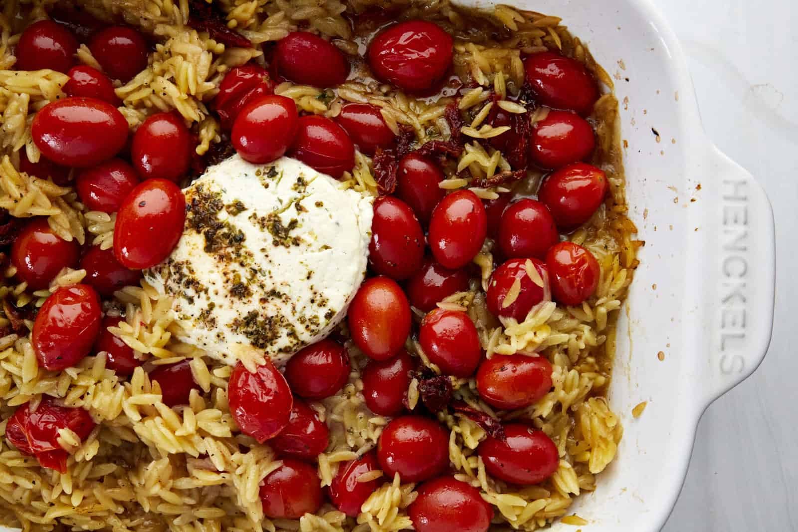 Uncooked pasta, tomatoes, cheese, and herbs in a baking dish.