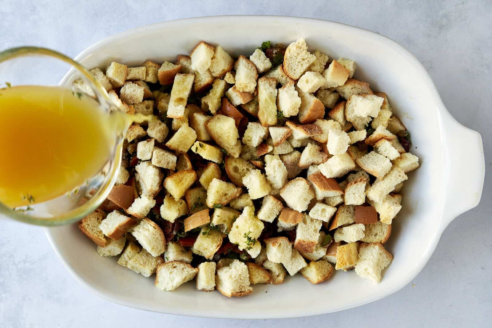 Chicken broth being poured over unbaked bread dressing.