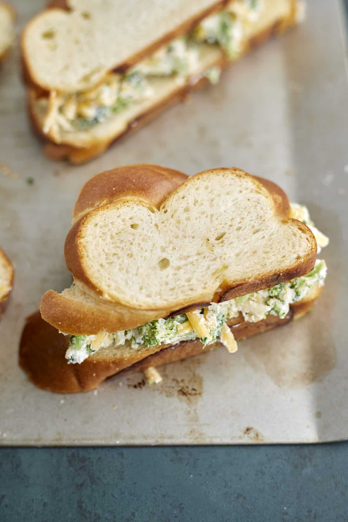Uncooked grilled cheese sandwiches with broccoli on a baking sheet.