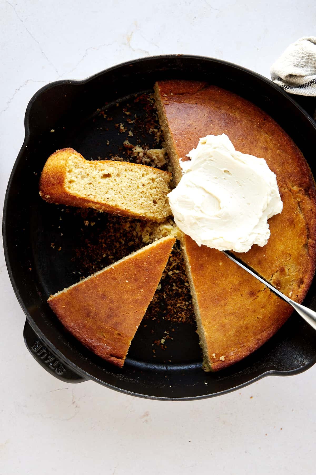 Half a skillet of brown butter cornbread topped with whipped butter and two pieces on the other side.