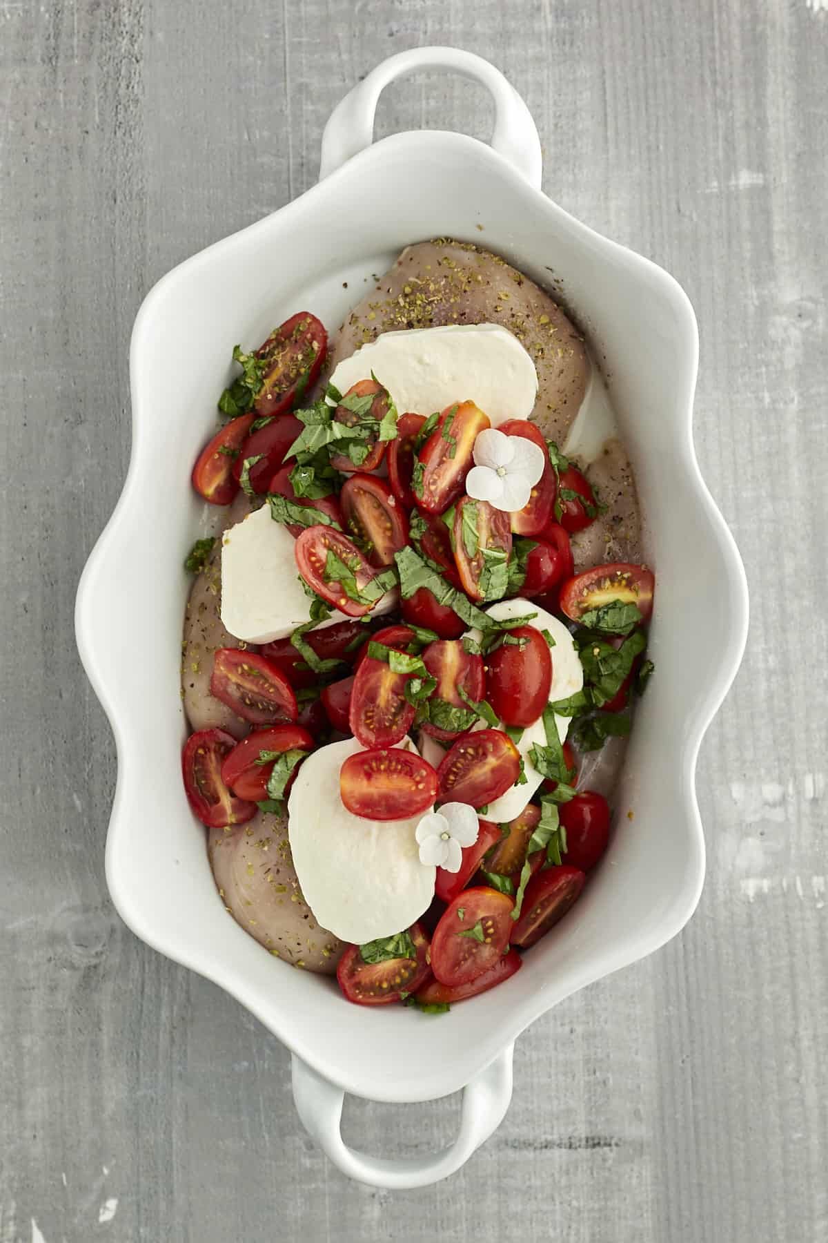raw chicken, fresh mozzarella, tomatoes, and basil in a white baking dish