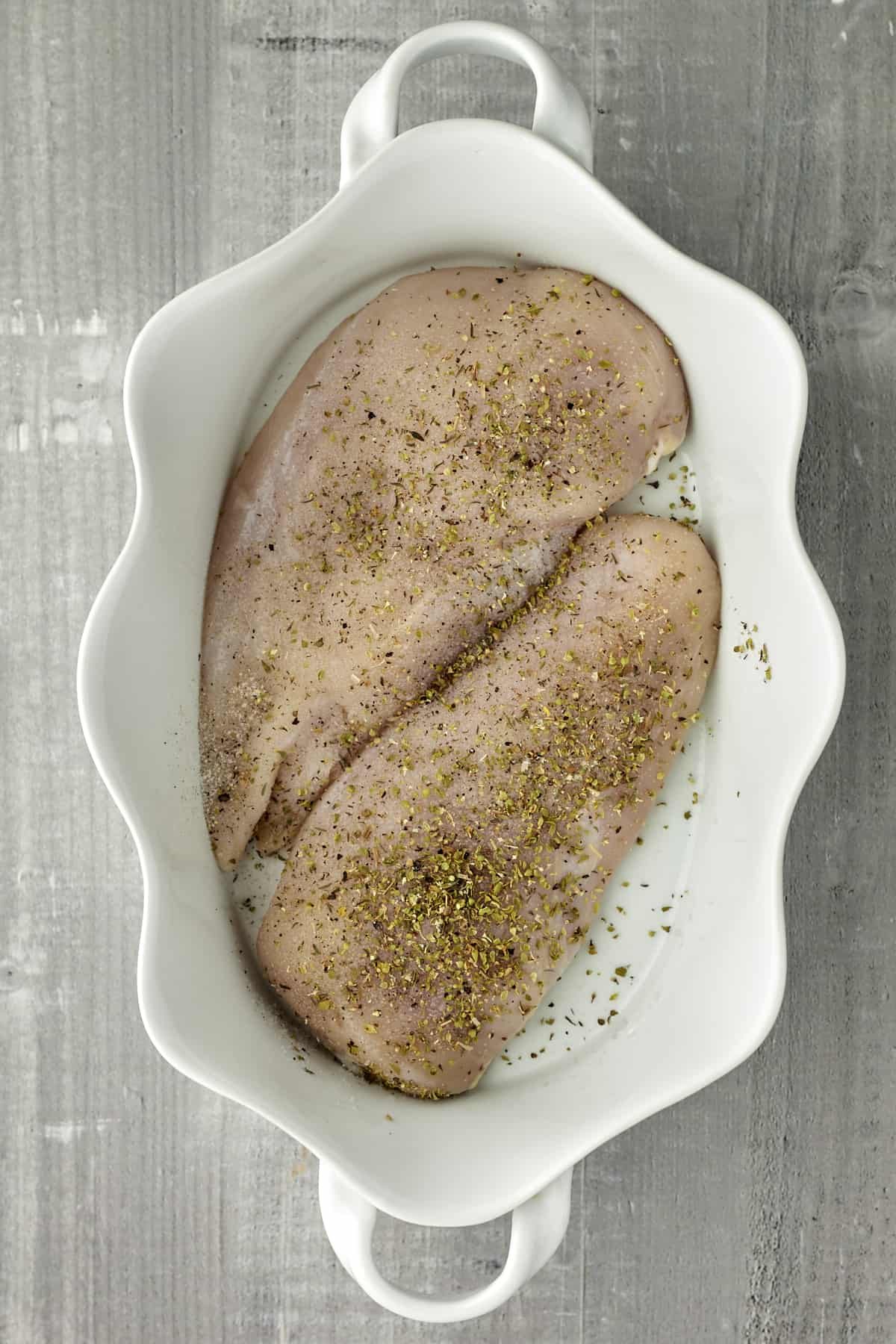 seasoned raw chicken breasts in a white baking dish