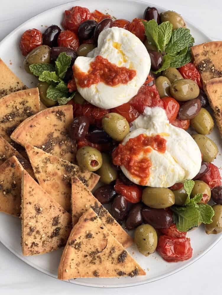 close up burrata with roasted tomatoes, olives and zaatar pita