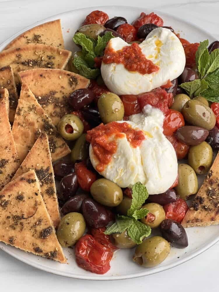 side view burrata with roasted tomatoes, olives and zaatar pita