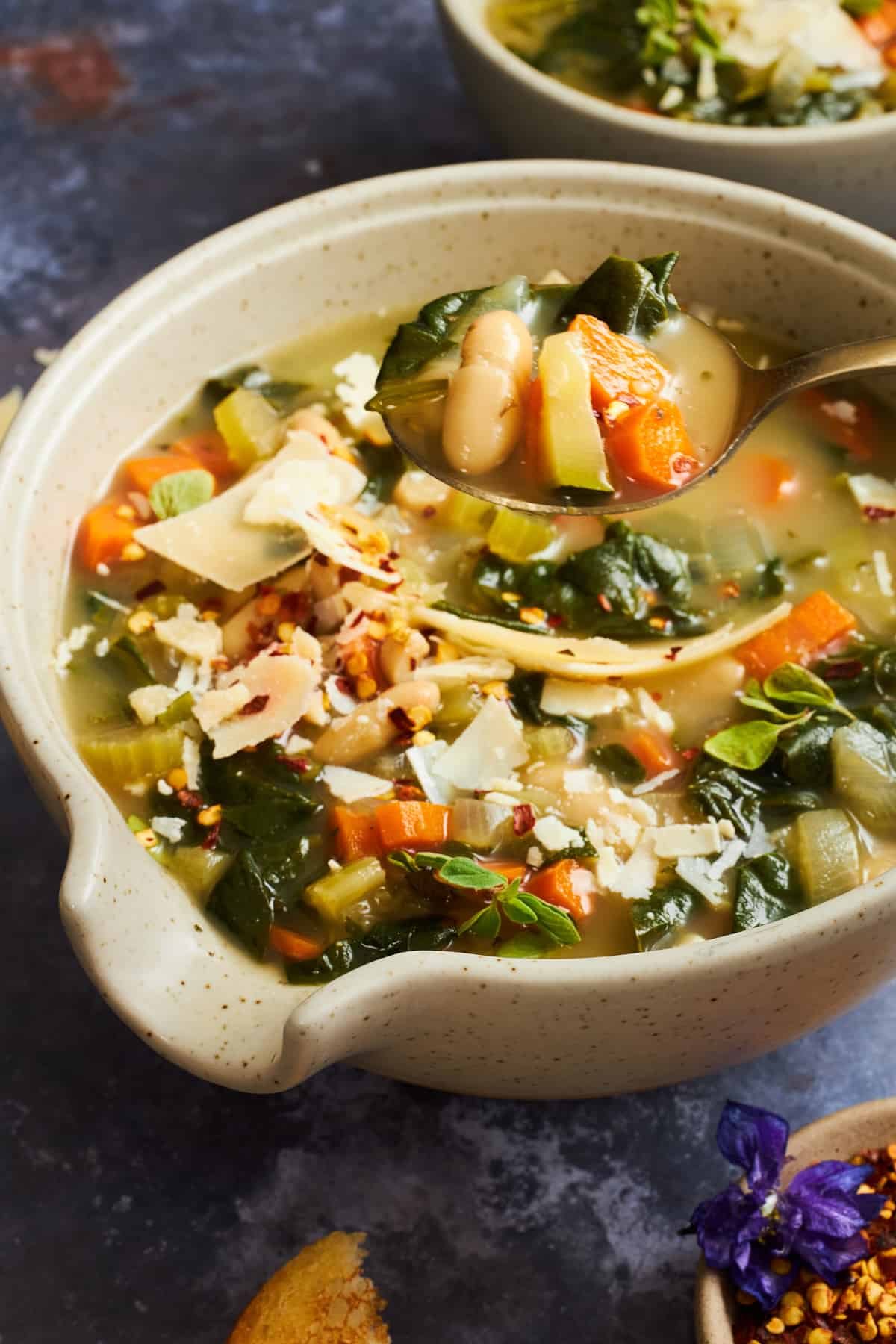 A spoon lifting a bite from a bowl of white bean soup.