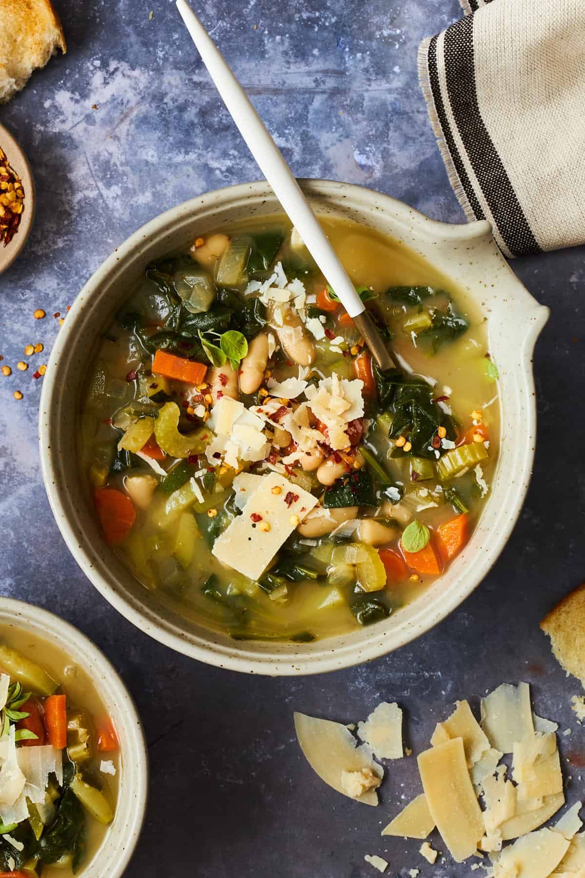A bowl of cannellini bean soup with vegetables topped with parmesan.