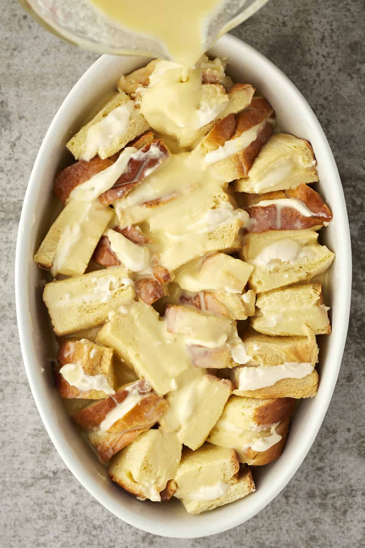 custard topping being poured over unbaked cannoli french toast.
