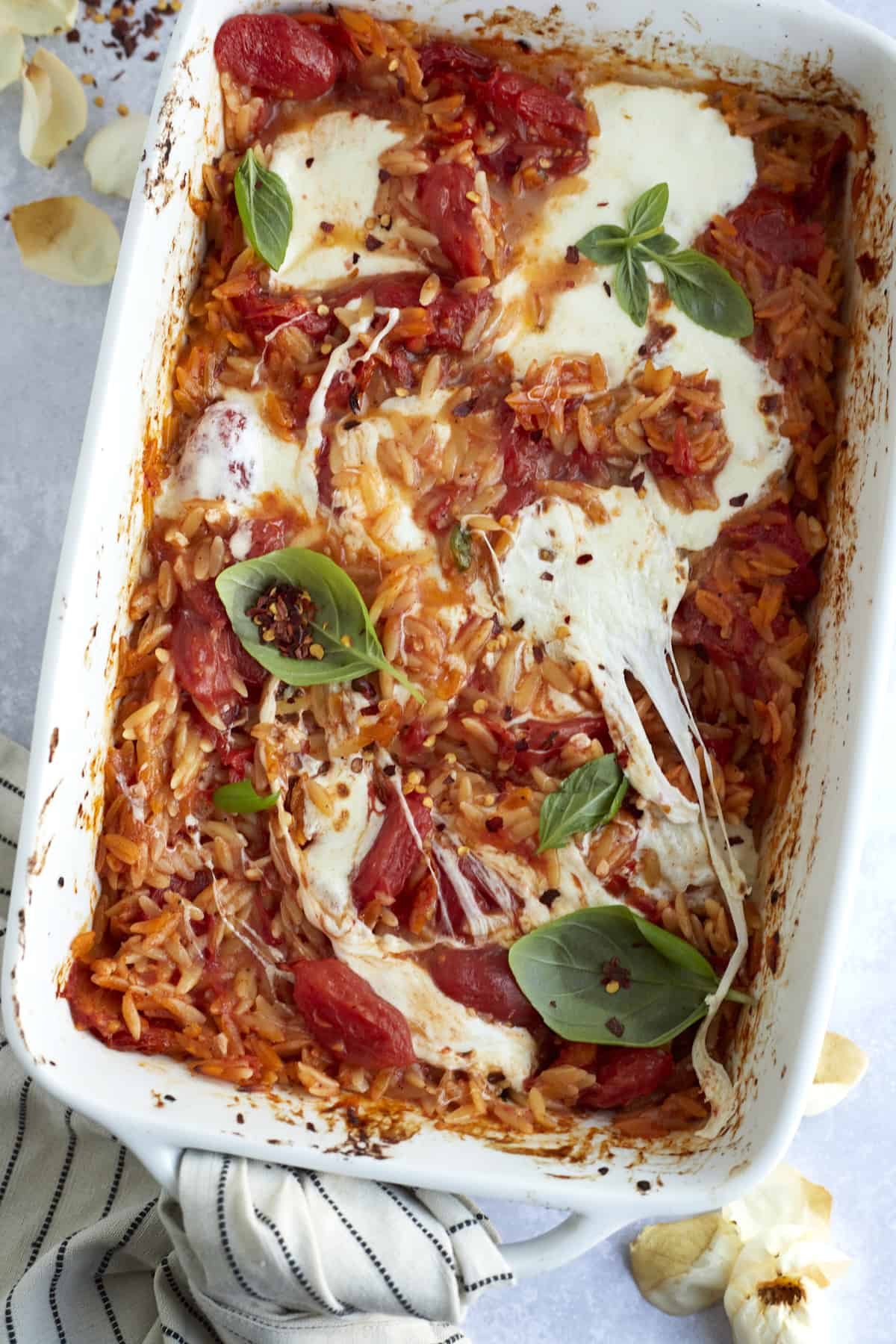 overhead image of caprese baked orzo pasta in a casserole dish with melted mozzarella on top