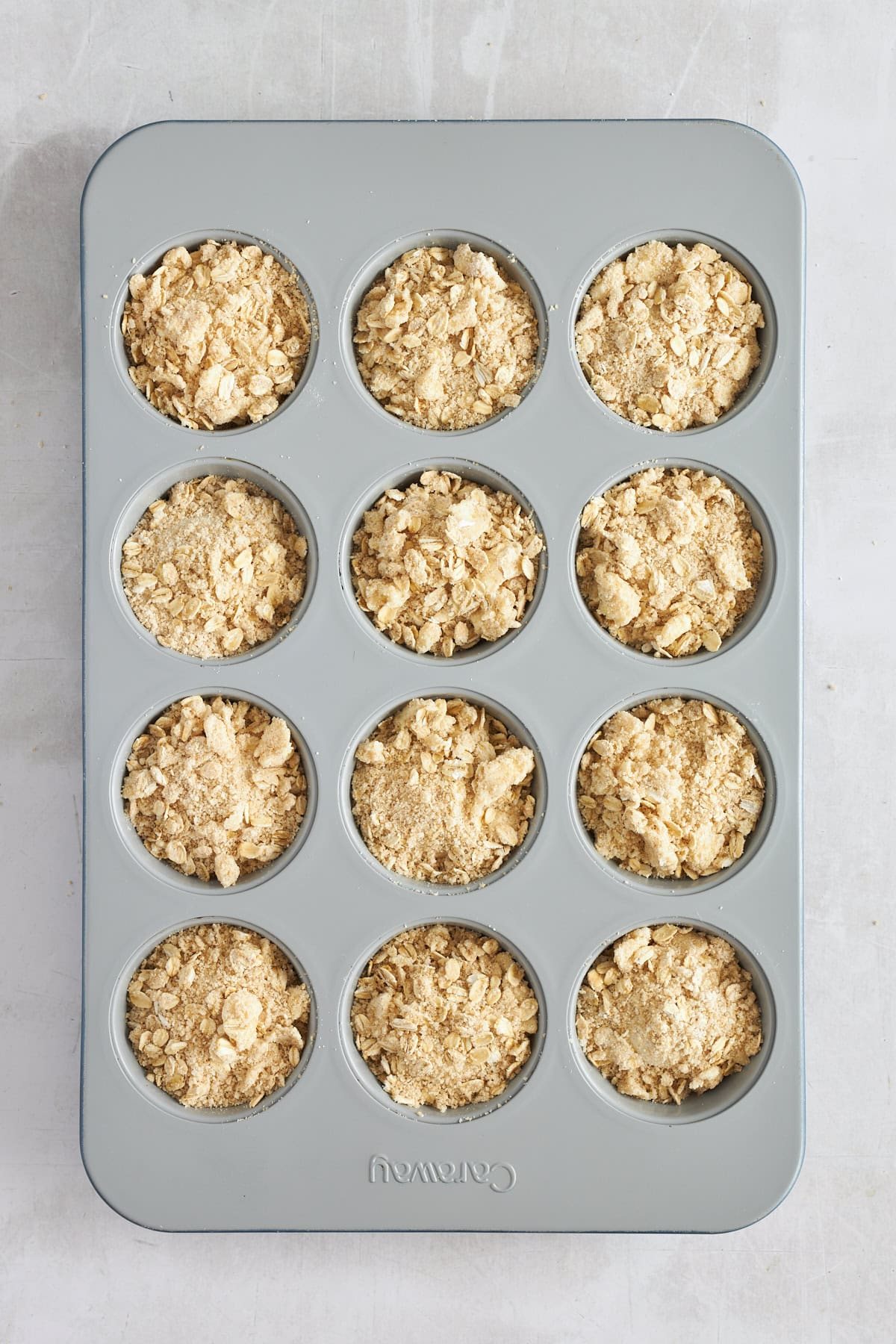 Raw dinner rolls topped with an oat crumble in a muffin tin.
