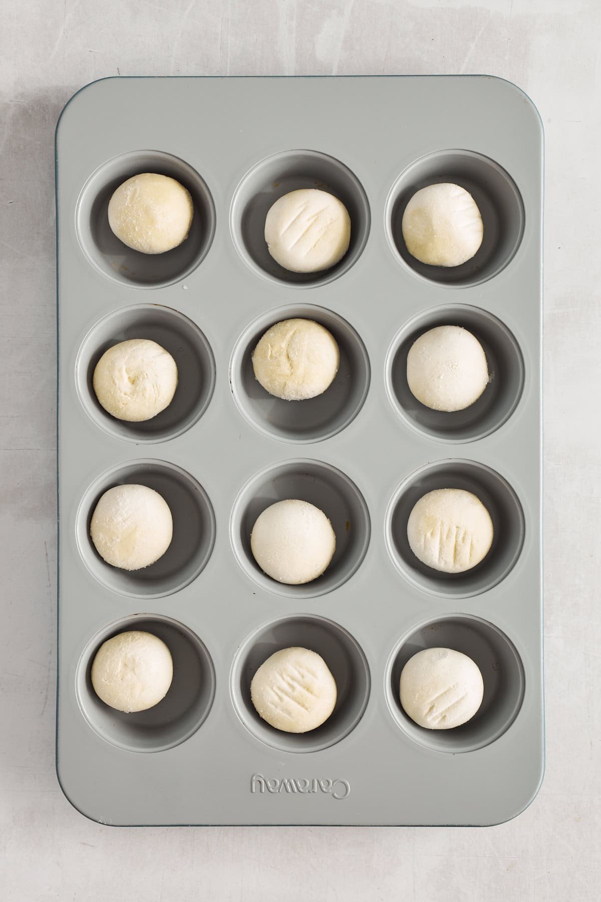 Raw dinner rolls in a muffin tin.