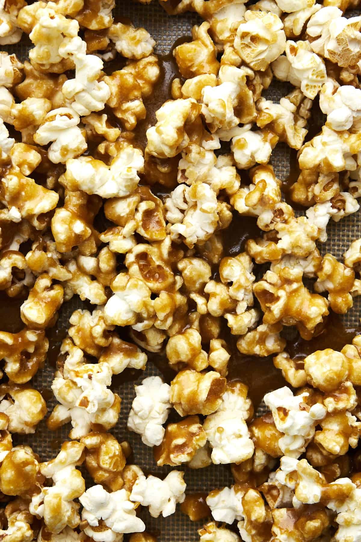Caramel sauce poured over popped popcorn on a baking sheet.