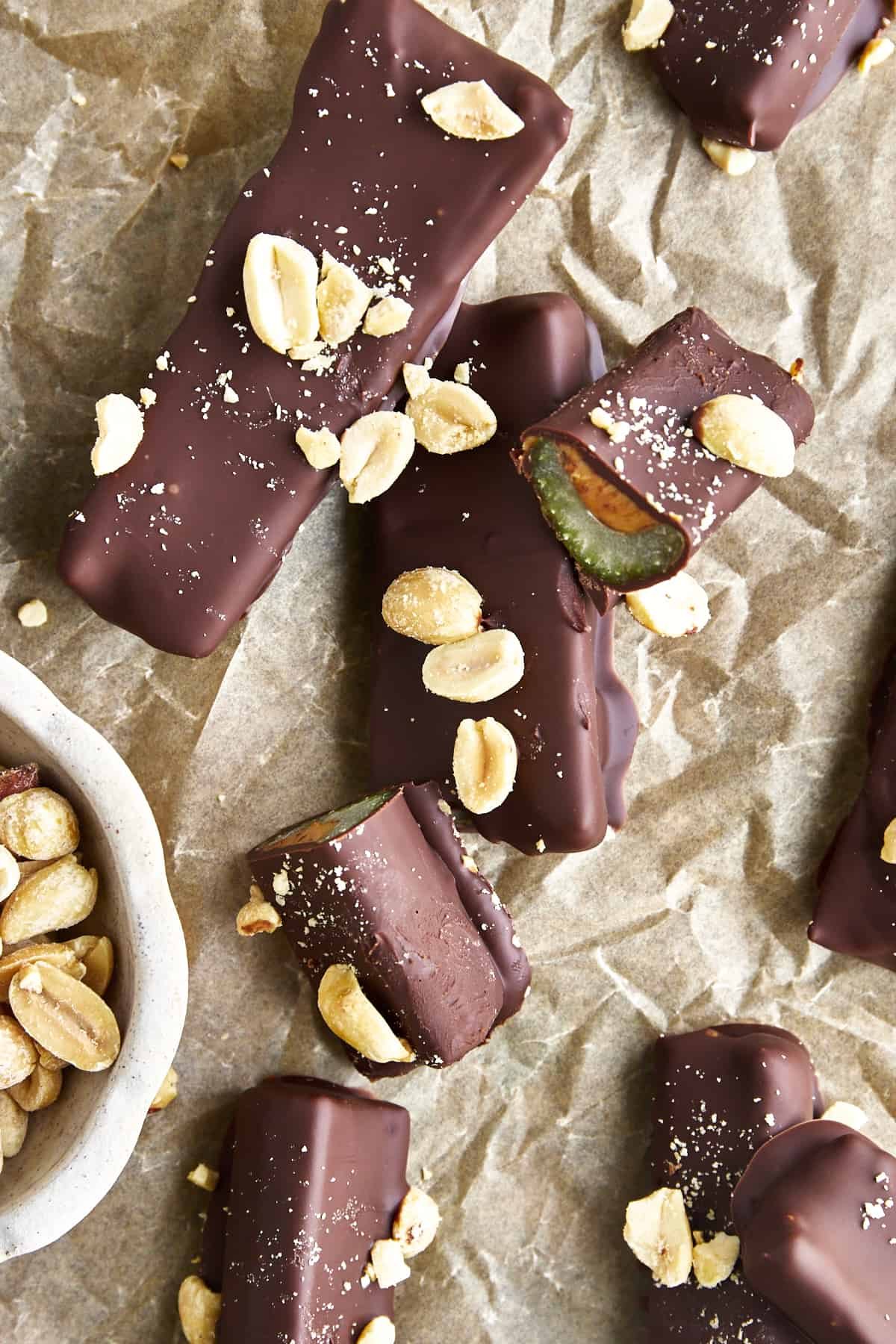 Chocolate dipped celery and peanut butter logs topped withe peanuts and sea salt on parchment paper with one log sliced in half.
