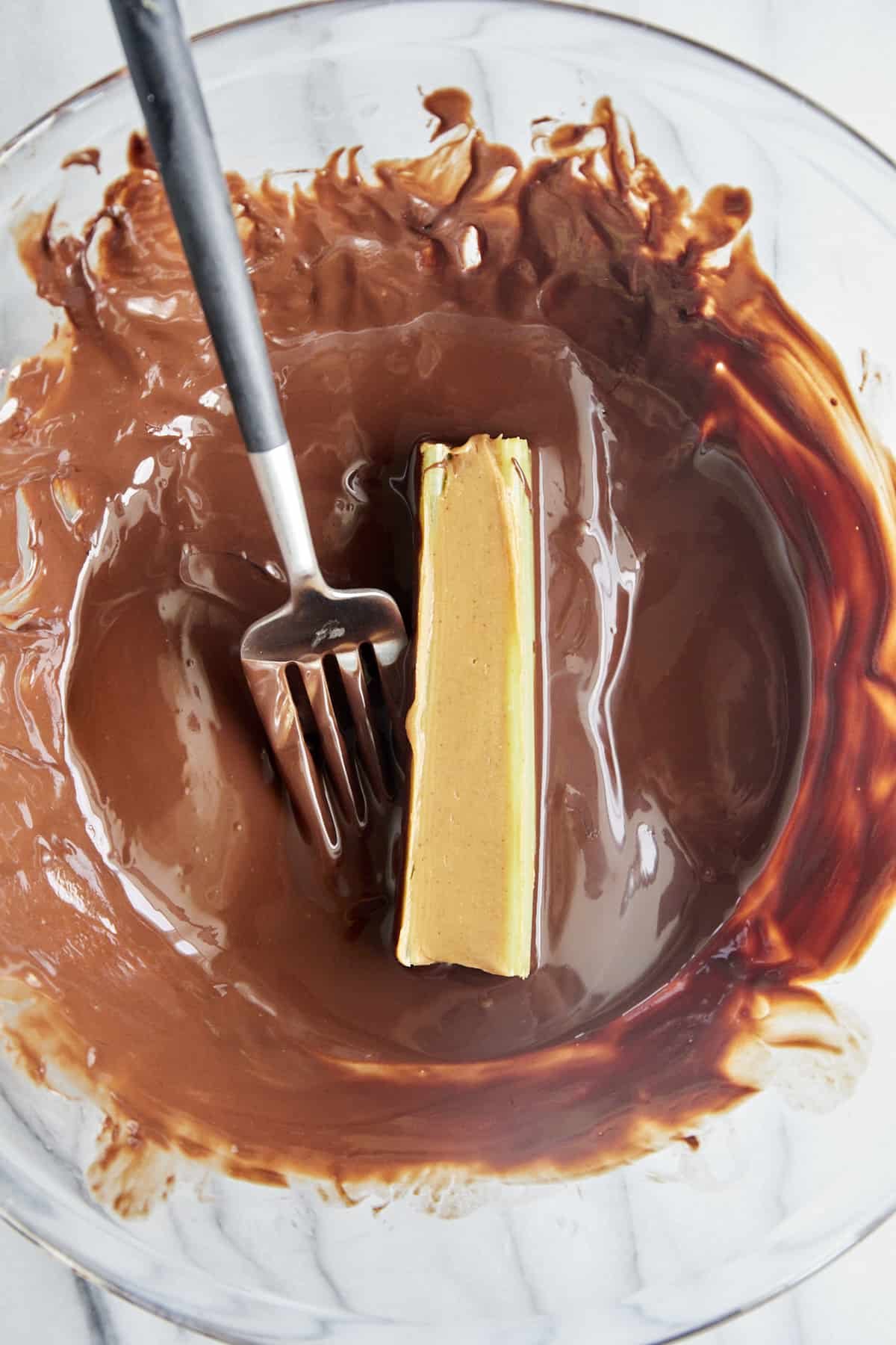 A peanut butter stuffed celery stick being rolled in melted chocolate.