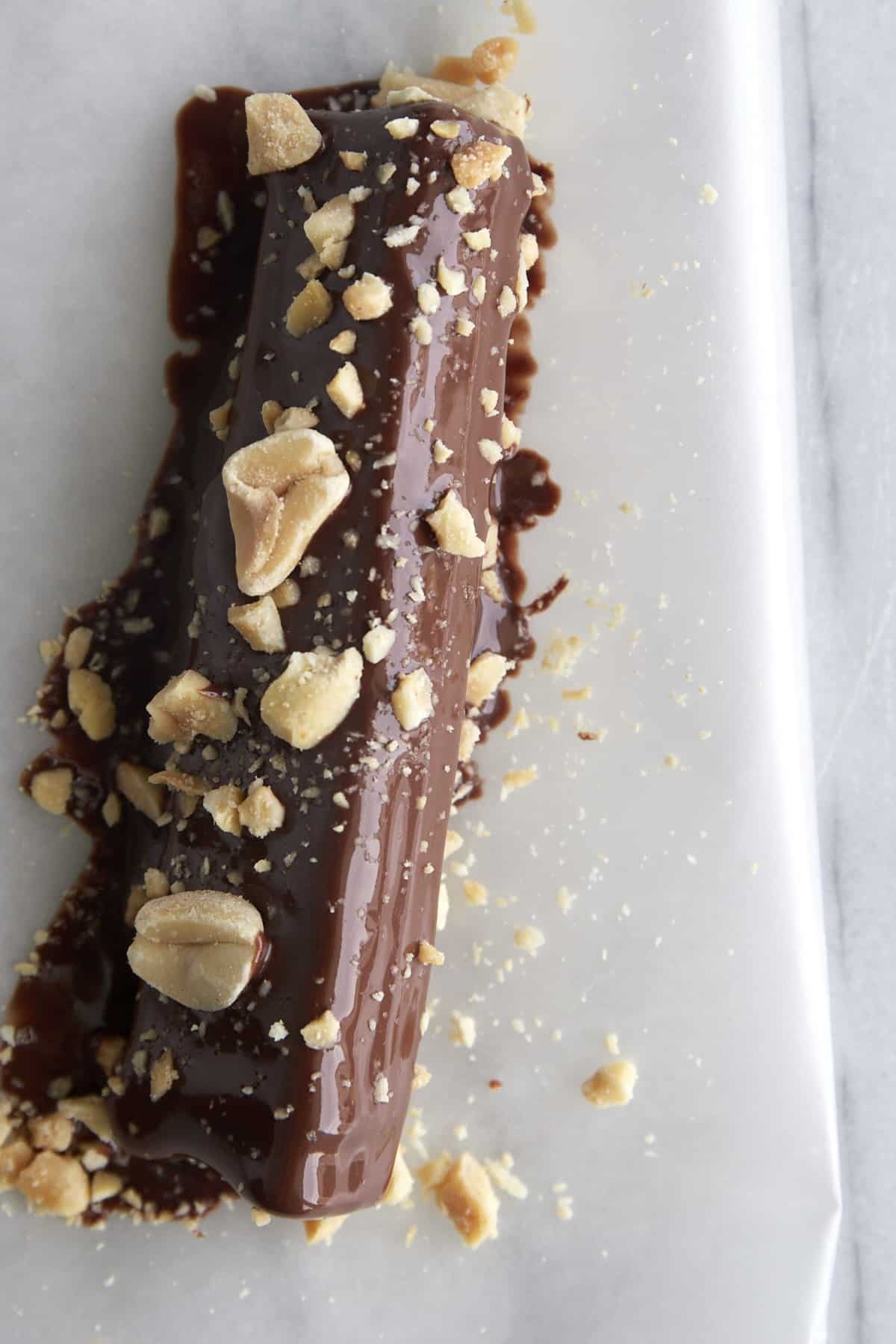 Overhead image of a celery stick coated with wet chocolate set on a piece of parchment paper to dry.