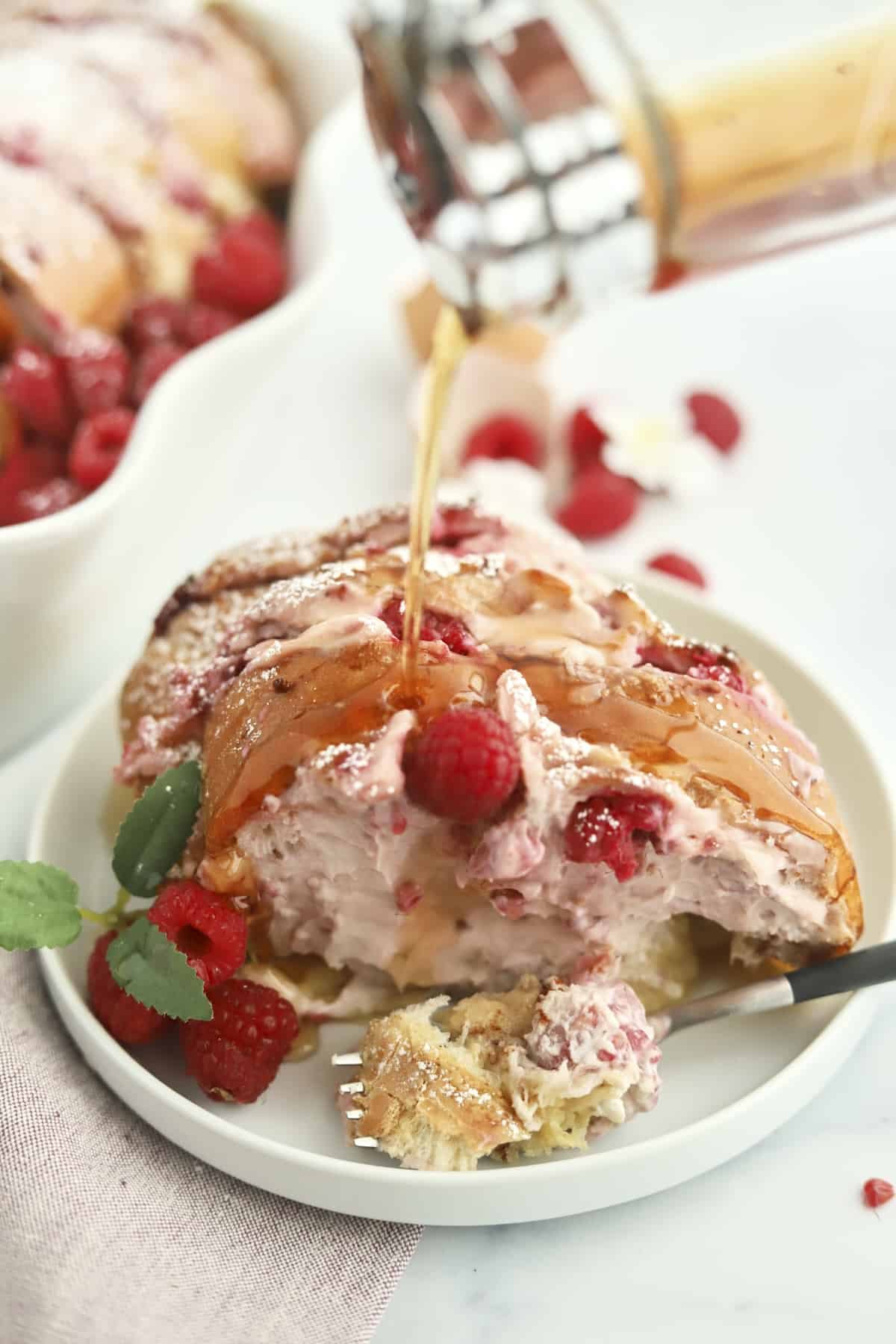 a serving of raspberry cheesecake challah french toast on a plate with syrup being poured on top