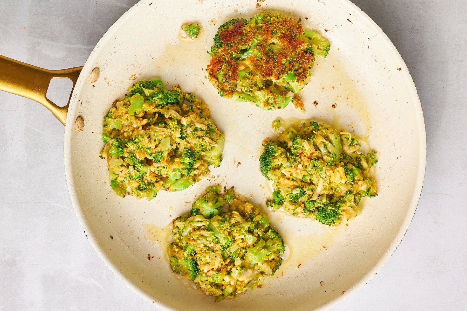Four cheesy broccoli fritters in a skillet.
