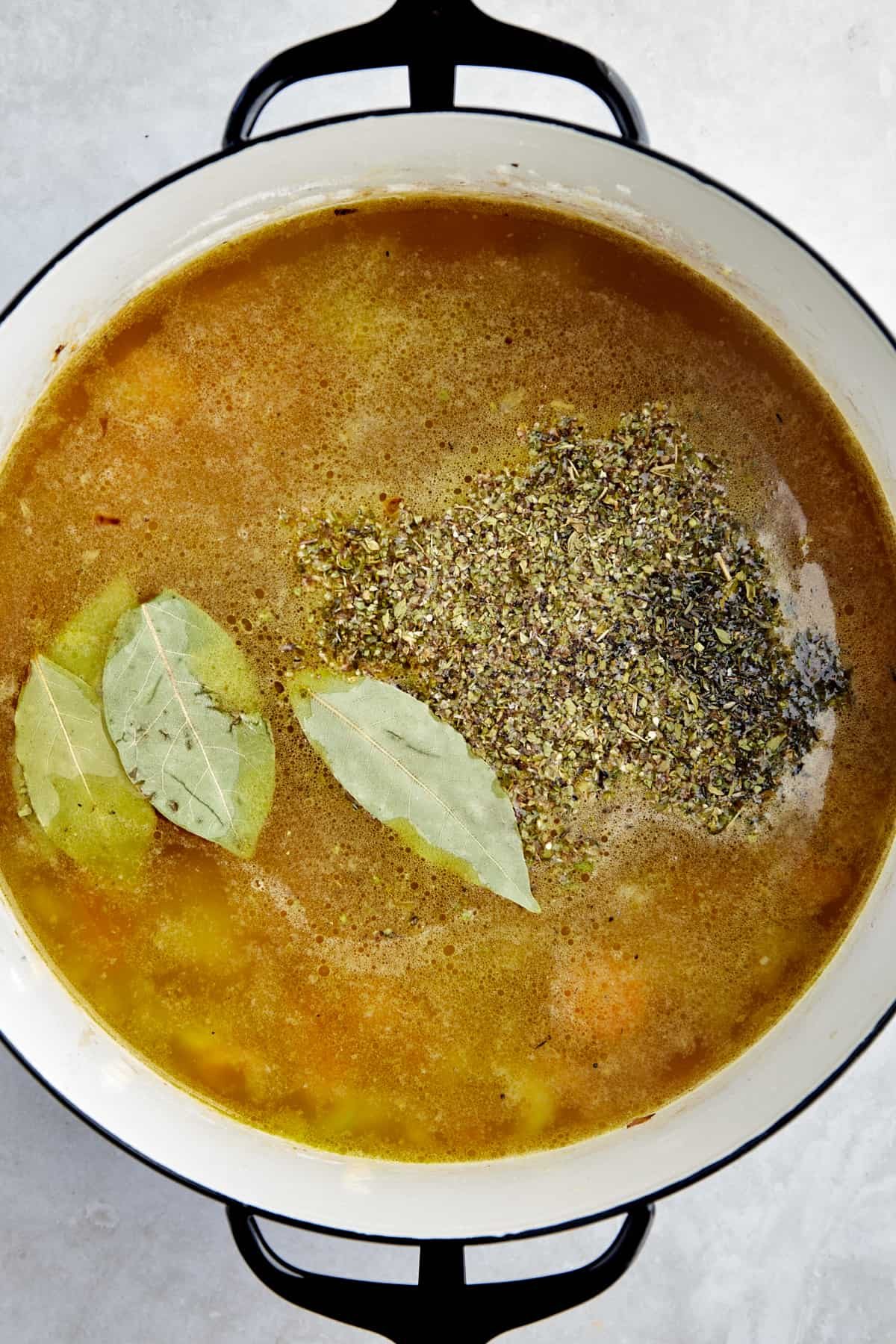 Vegetables, broth, seasonings, and bay leaves in a soup pot.