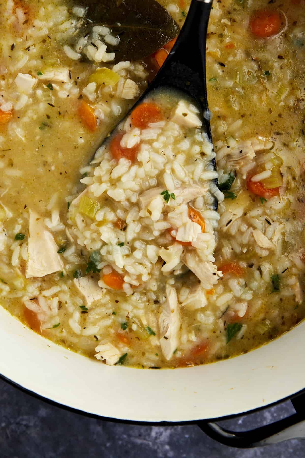A ladle lifting a portion of chicken and rice soup from a pot.