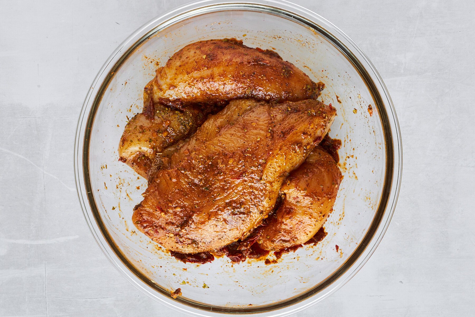 Raw chicken thighs tossed with seasonings in a bowl.