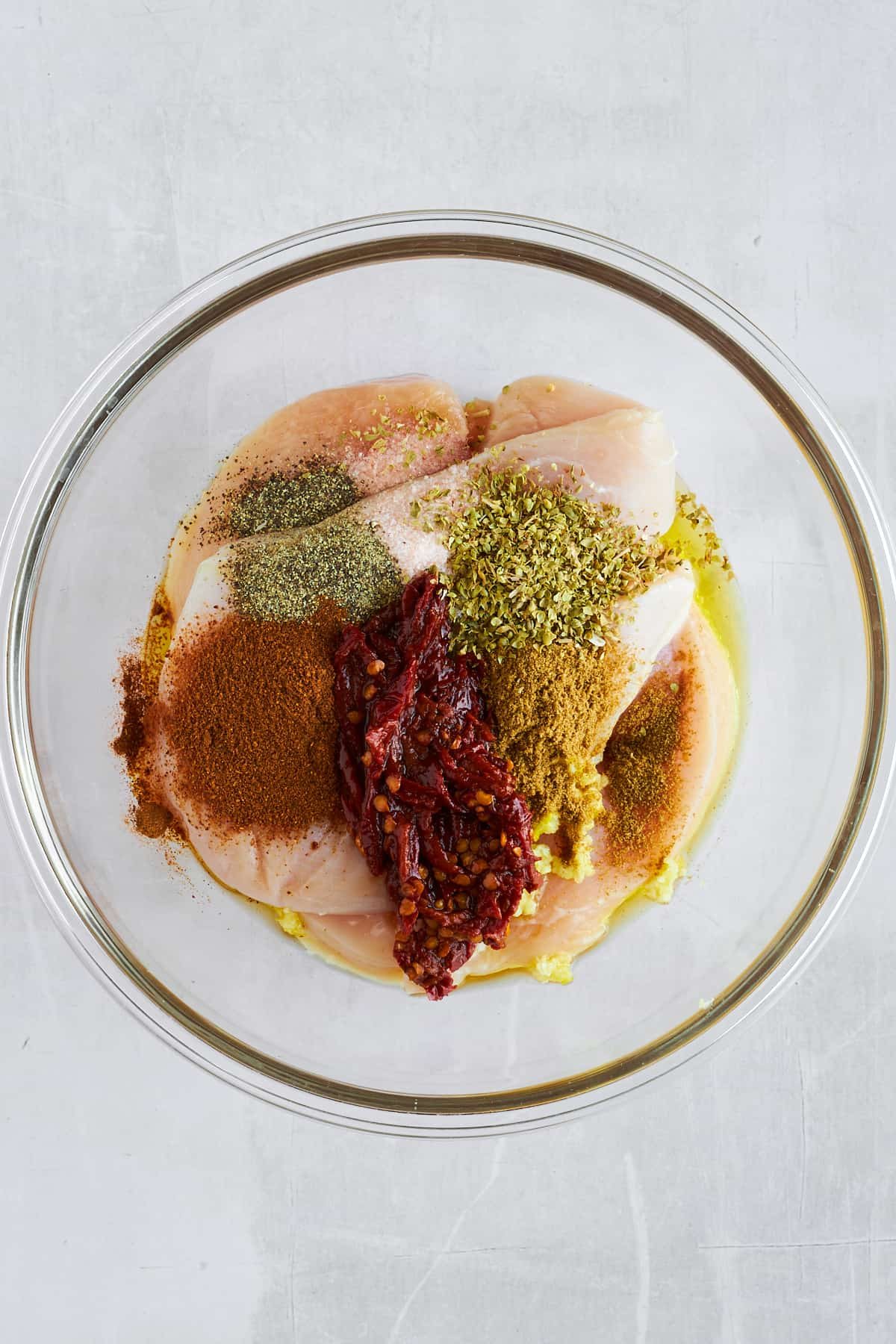 Raw chicken thighs topped with seasonings and oil in a bowl.