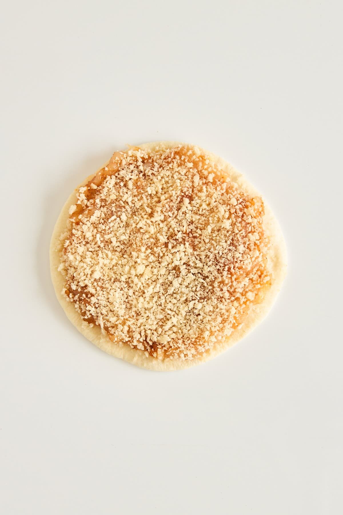 A round piece of dough topped with a crumbly brown sugar and cinnamon mixture, placed on a plain white background.