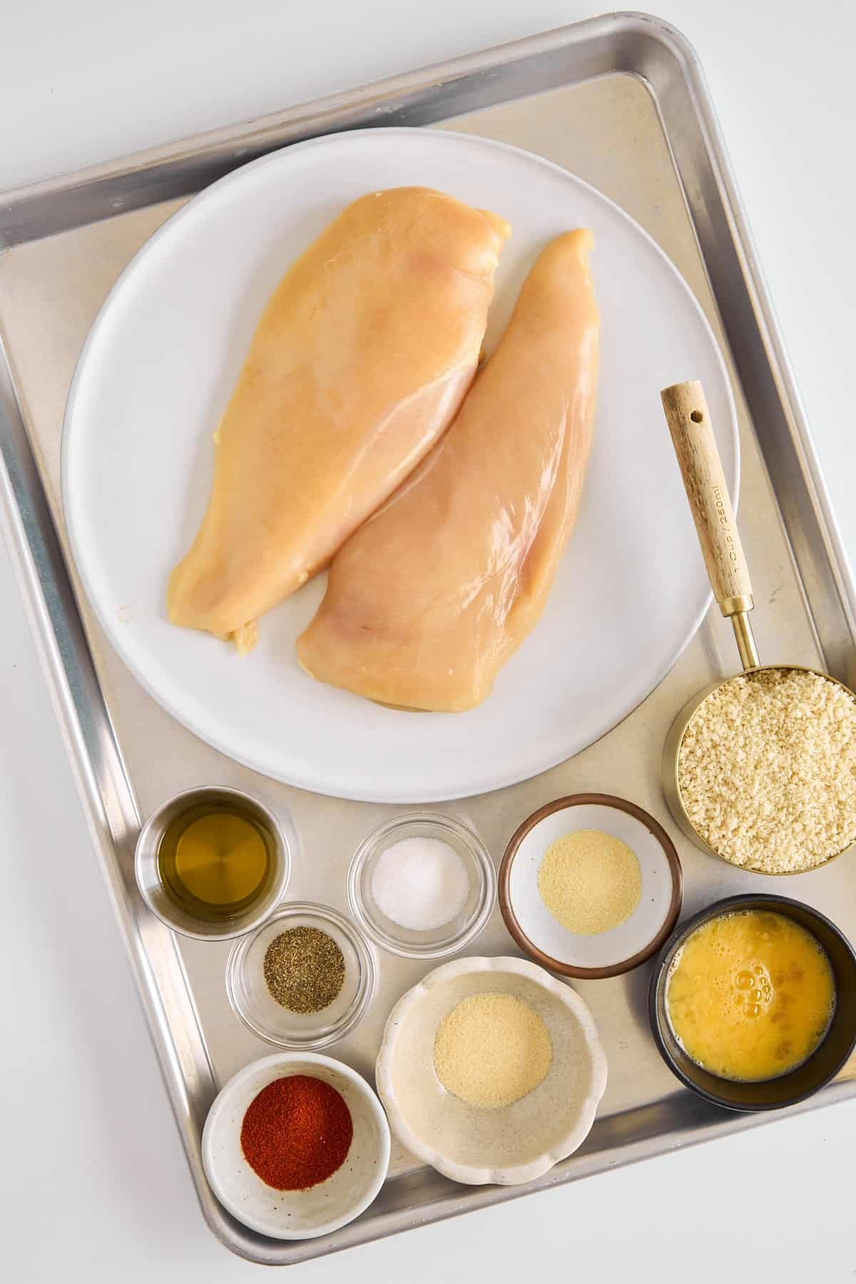 A plate of raw chicken breasts and various spices.