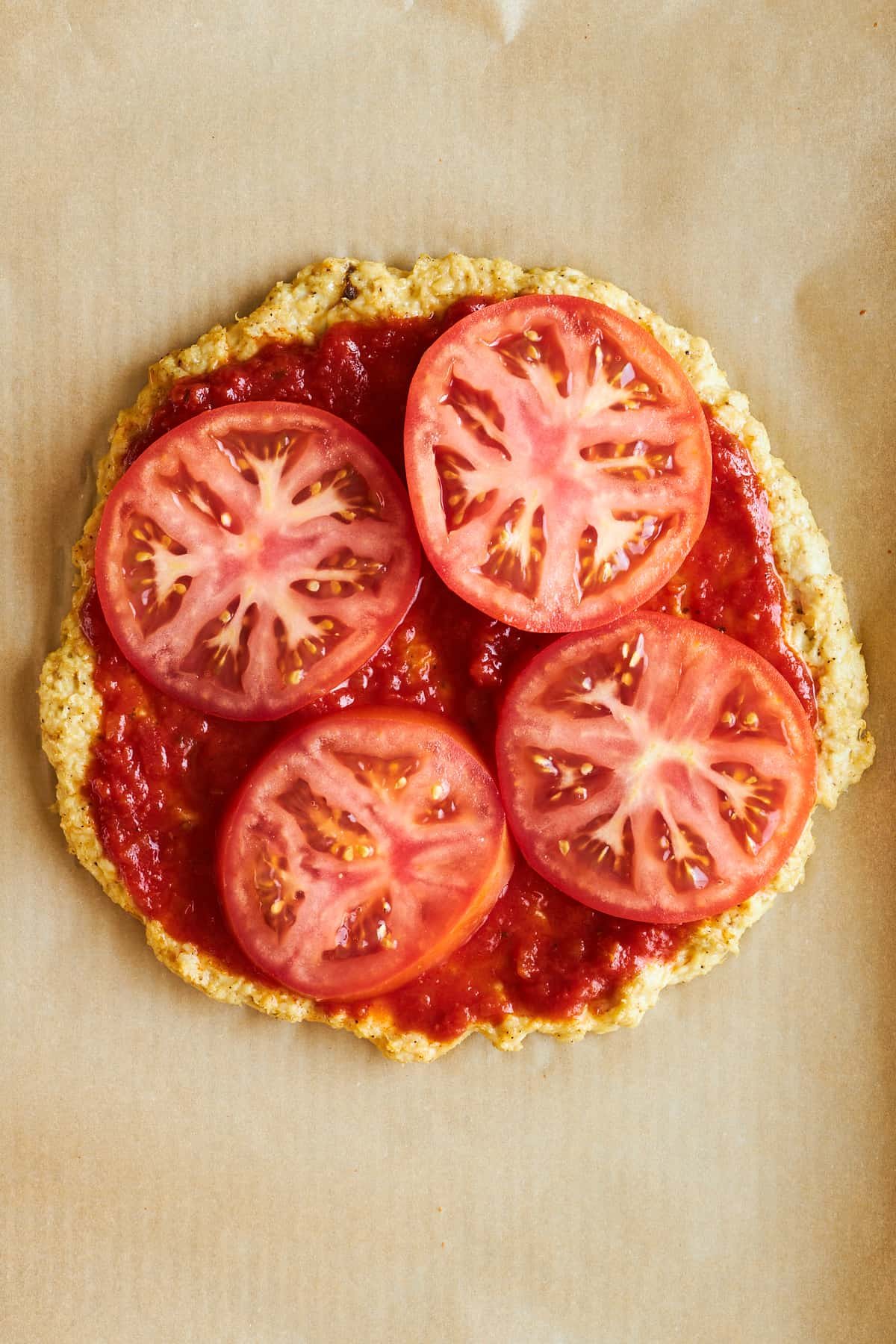 Chicken pizza crust topped with marinara sauce and tomatoes.