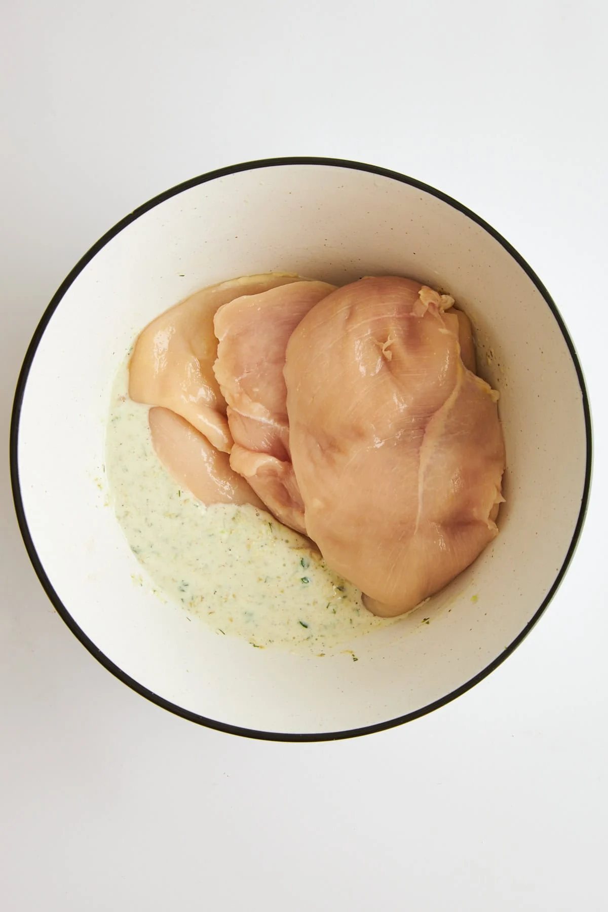 A bowl of tzatziki marinade and raw chicken.