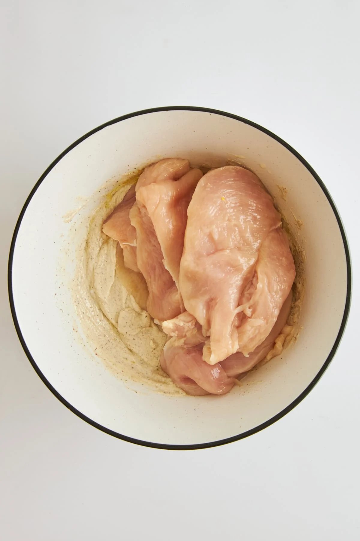Raw chicken and tahini yogurt marinade in a bowl.
