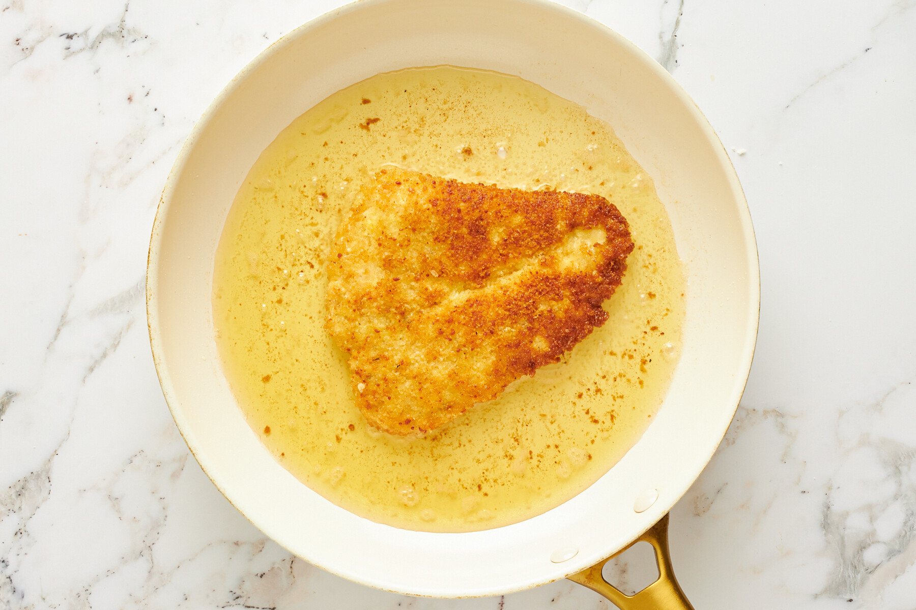 Breaded chicken cooking in oil in a skillet.