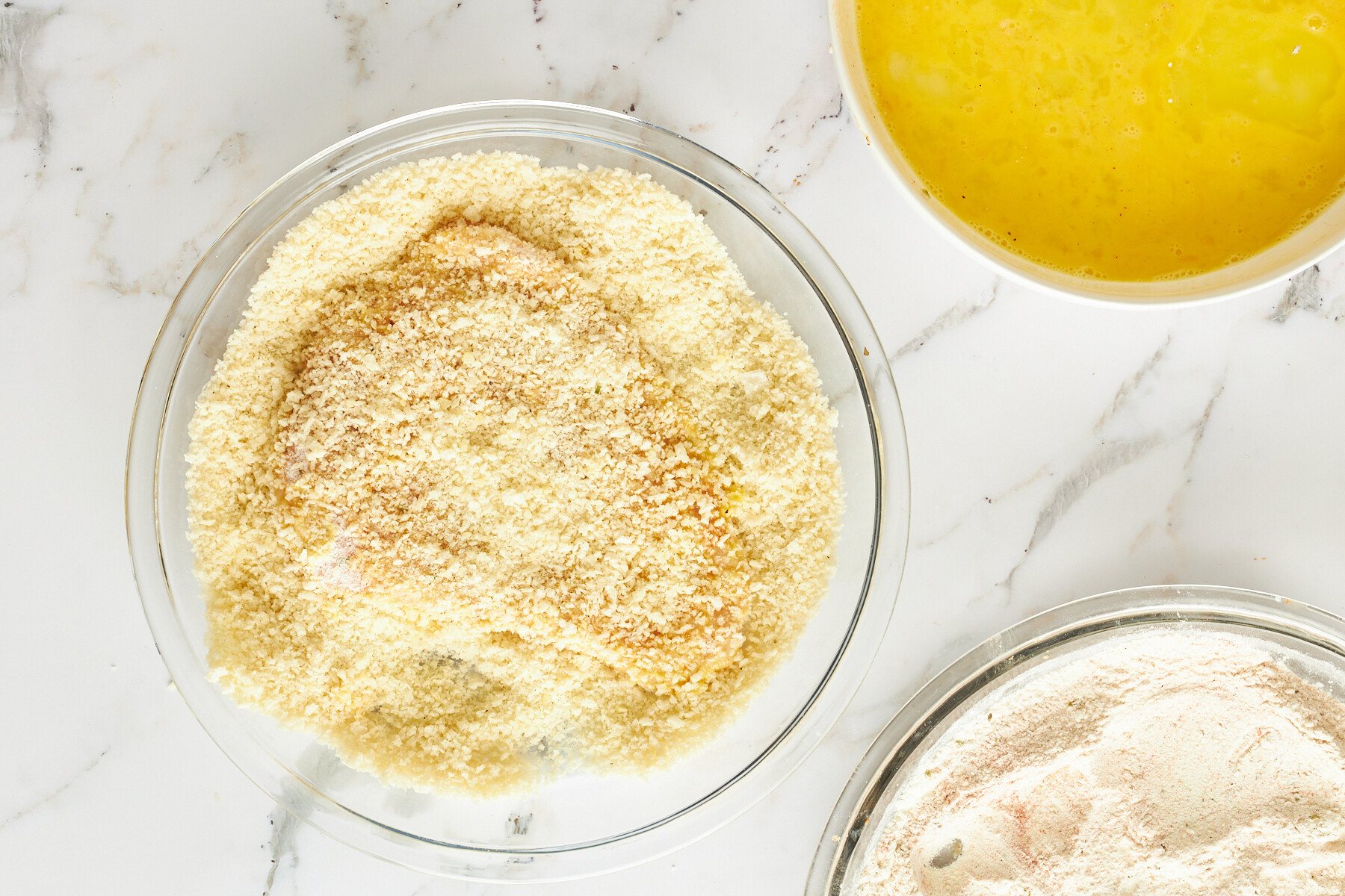 Raw breaded chicken in a bowl of breadcrumbs.
