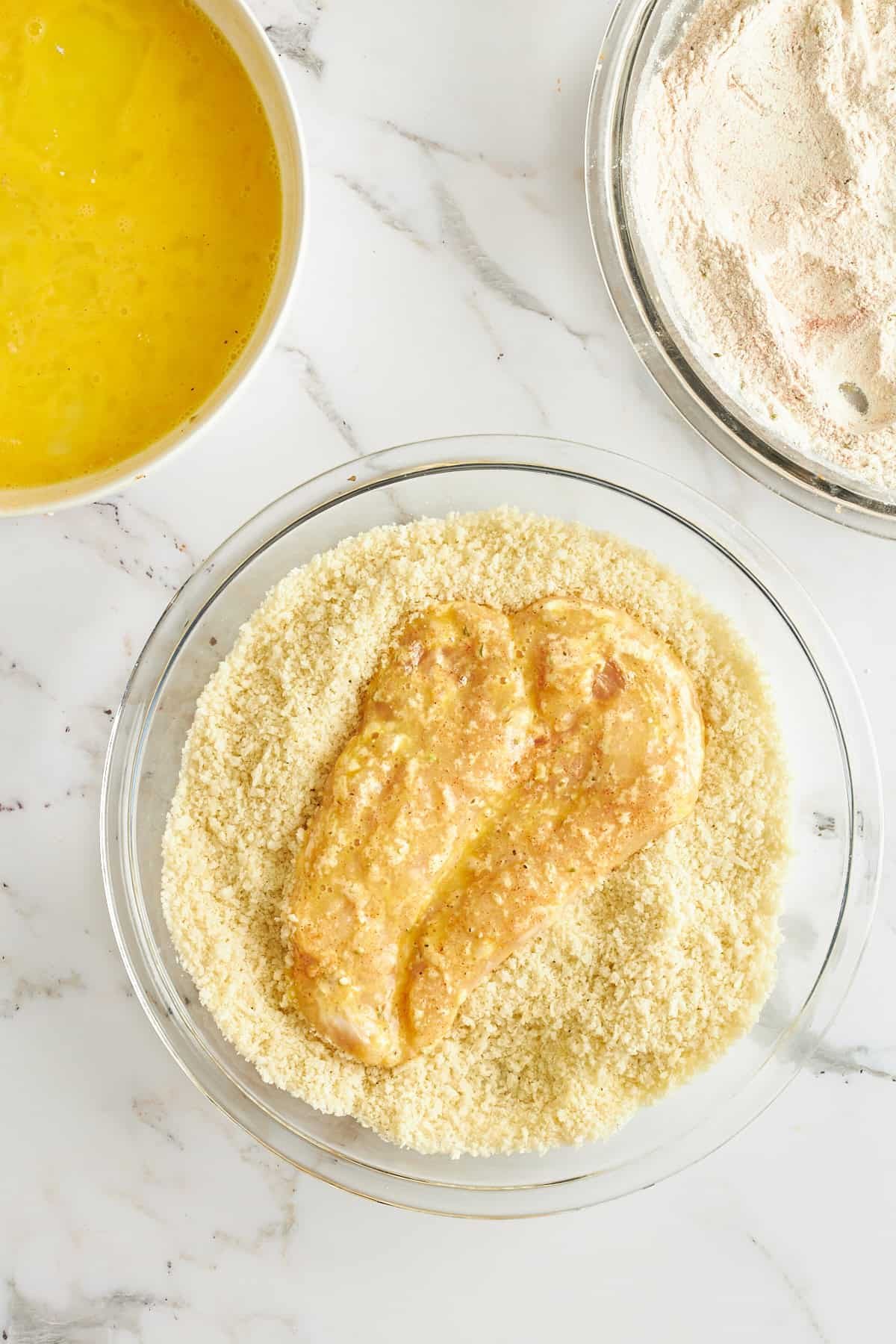 Raw breaded chicken in a bowl of breadcrumbs.