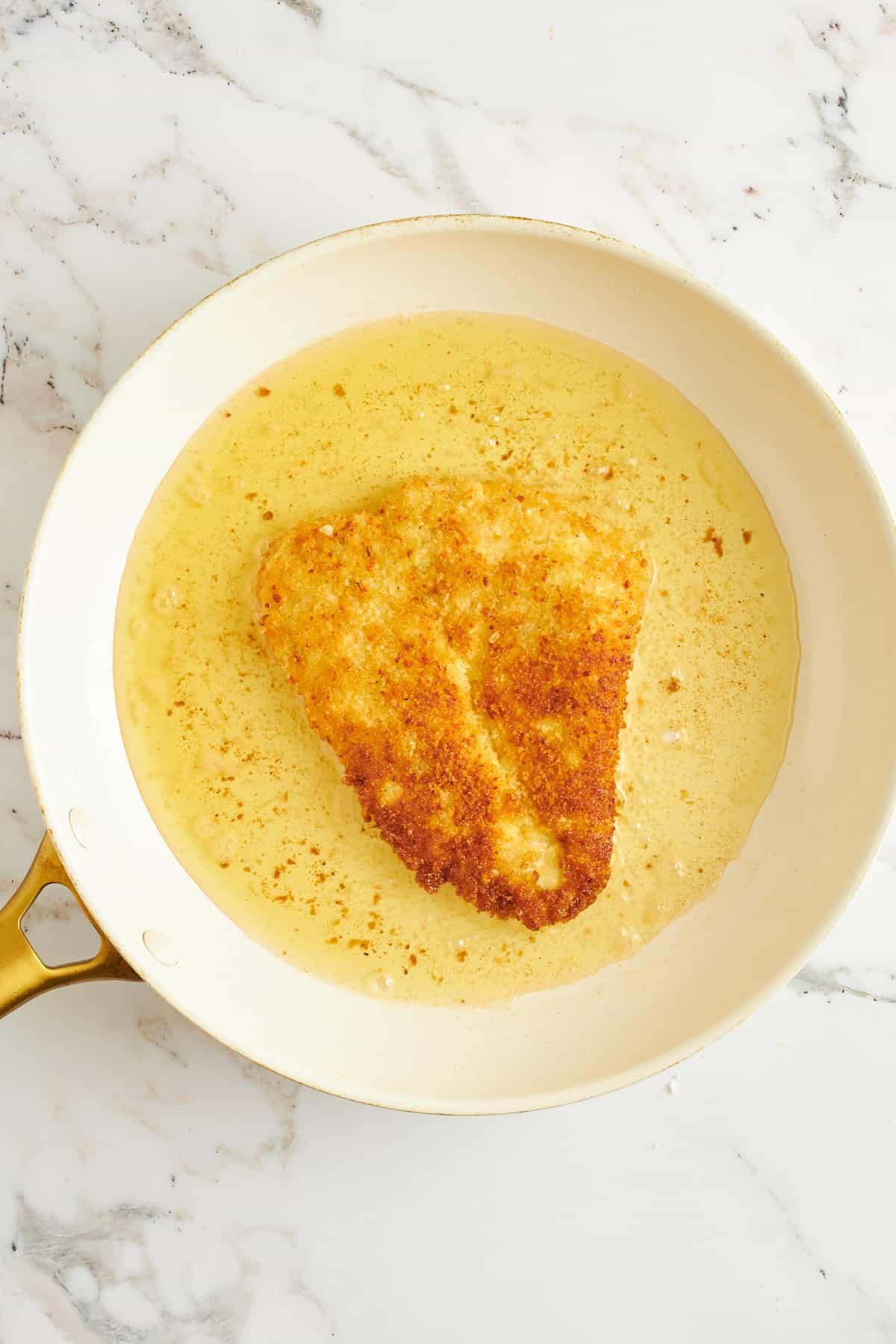 Breaded chicken breast cooking in oil in a skillet.