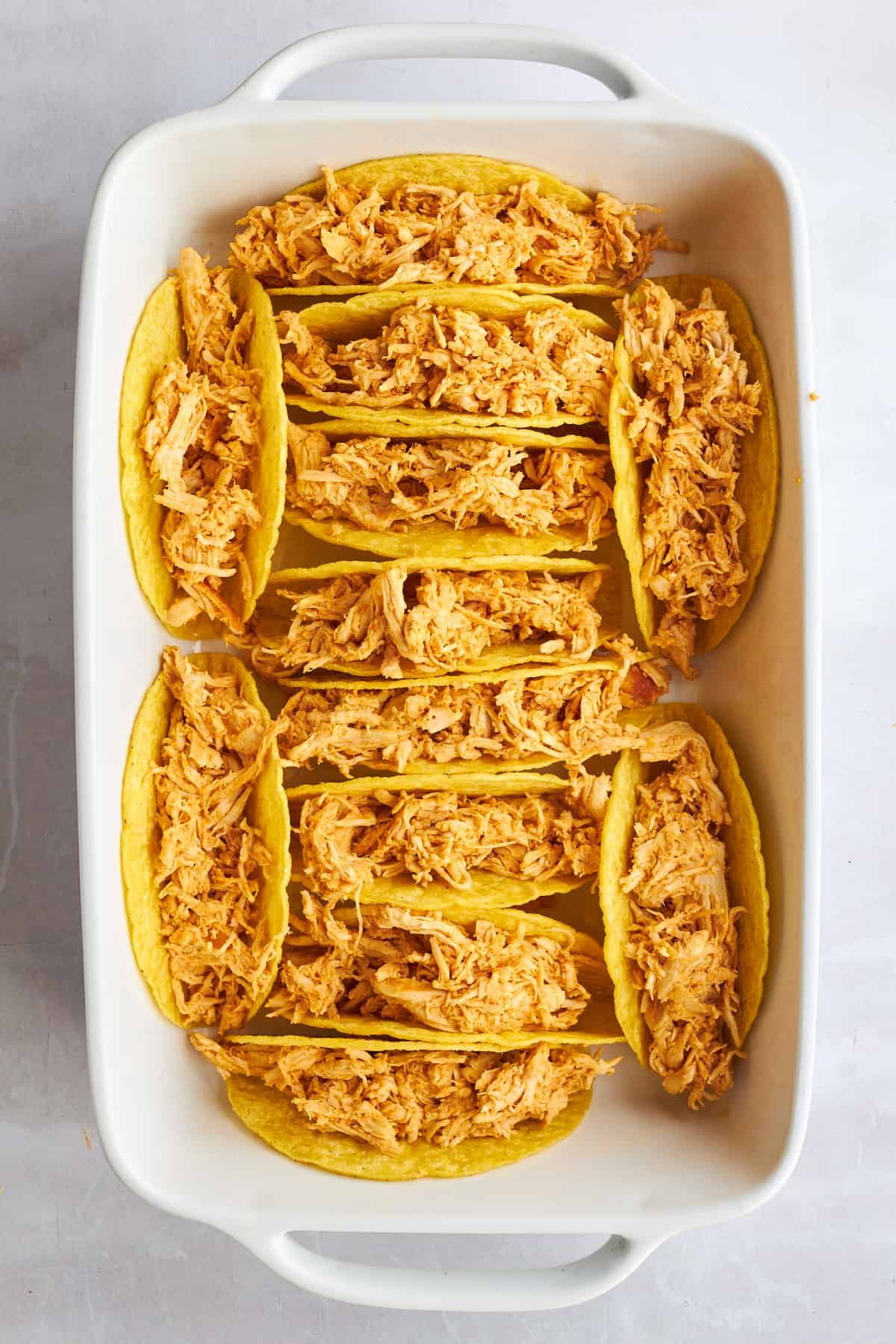 Shredded chicken shawarma stuffed in hard taco shells in a baking dish.