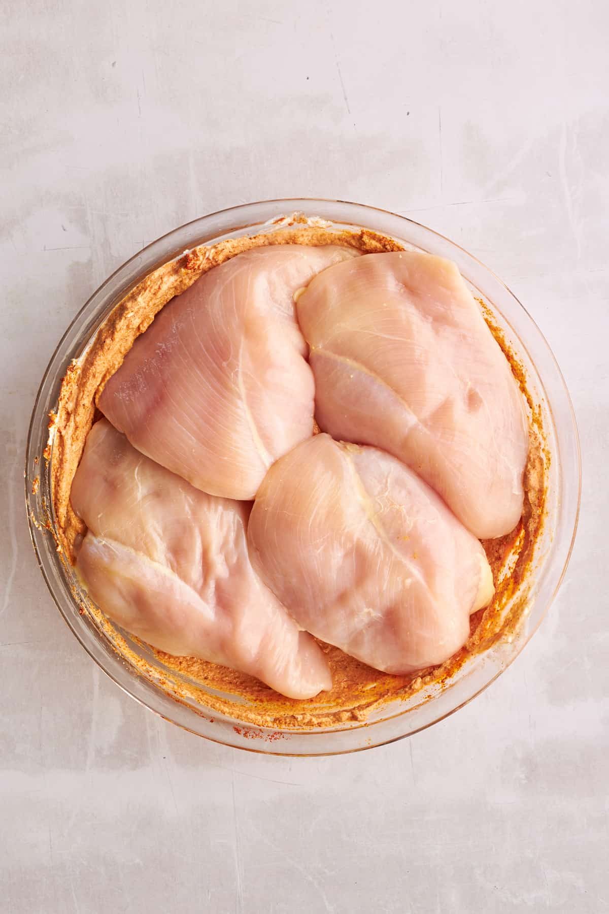 Raw chicken breasts in a bowl of shawarma marinade.