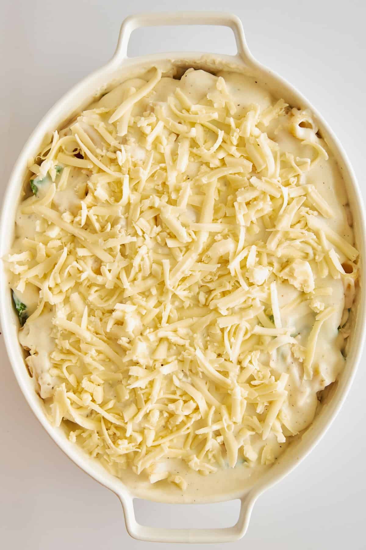 Uncooked Chicken Spinach Pasta Bake in a baking dish topped with cheese.