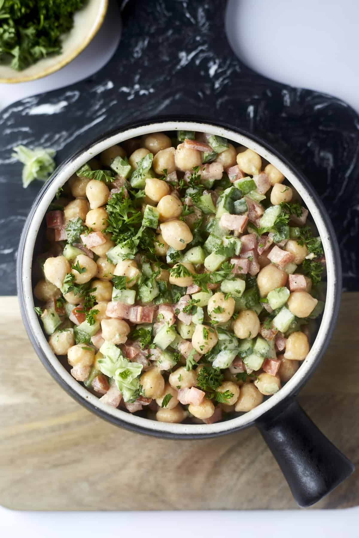 a bowl of chickpea and cucumber tahina salad topped with fresh parsley