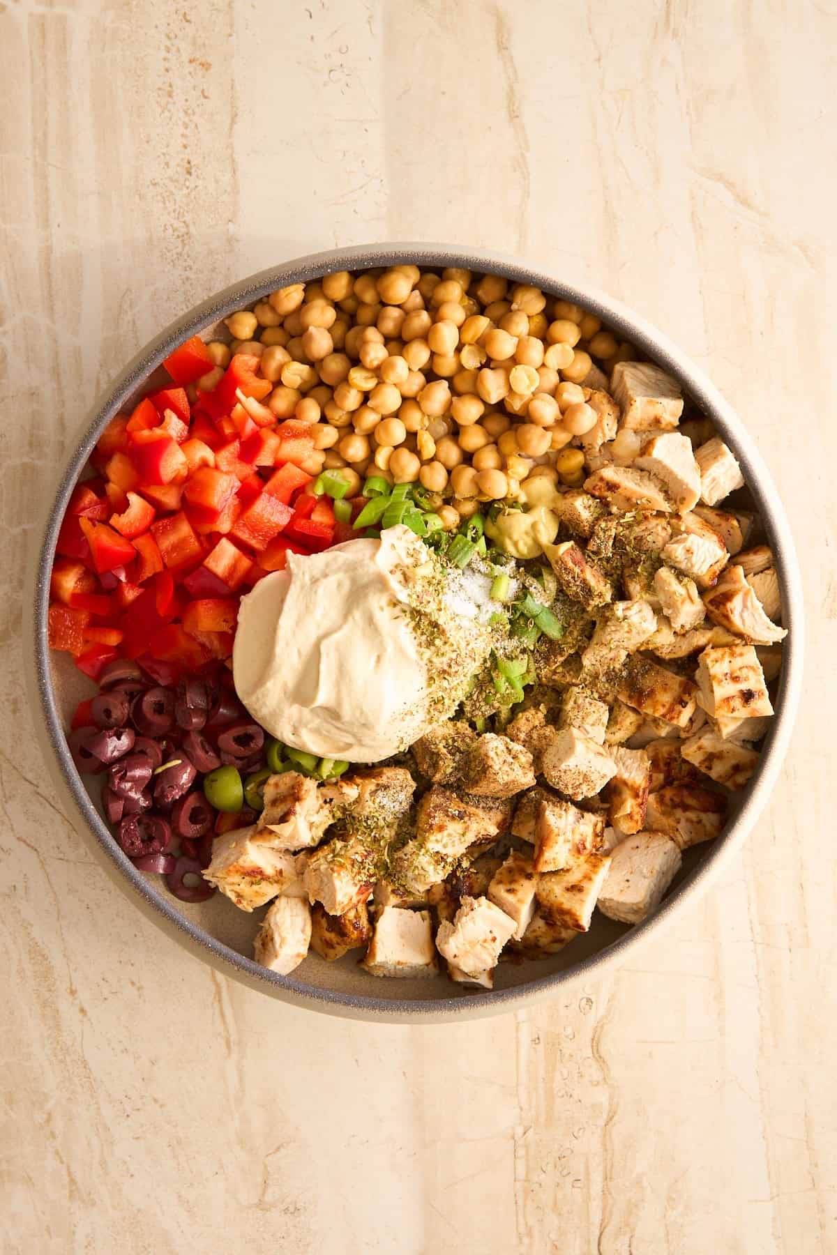 Chicken, olives, hummus, bell peppers, olives, and chickpeas before being combined.