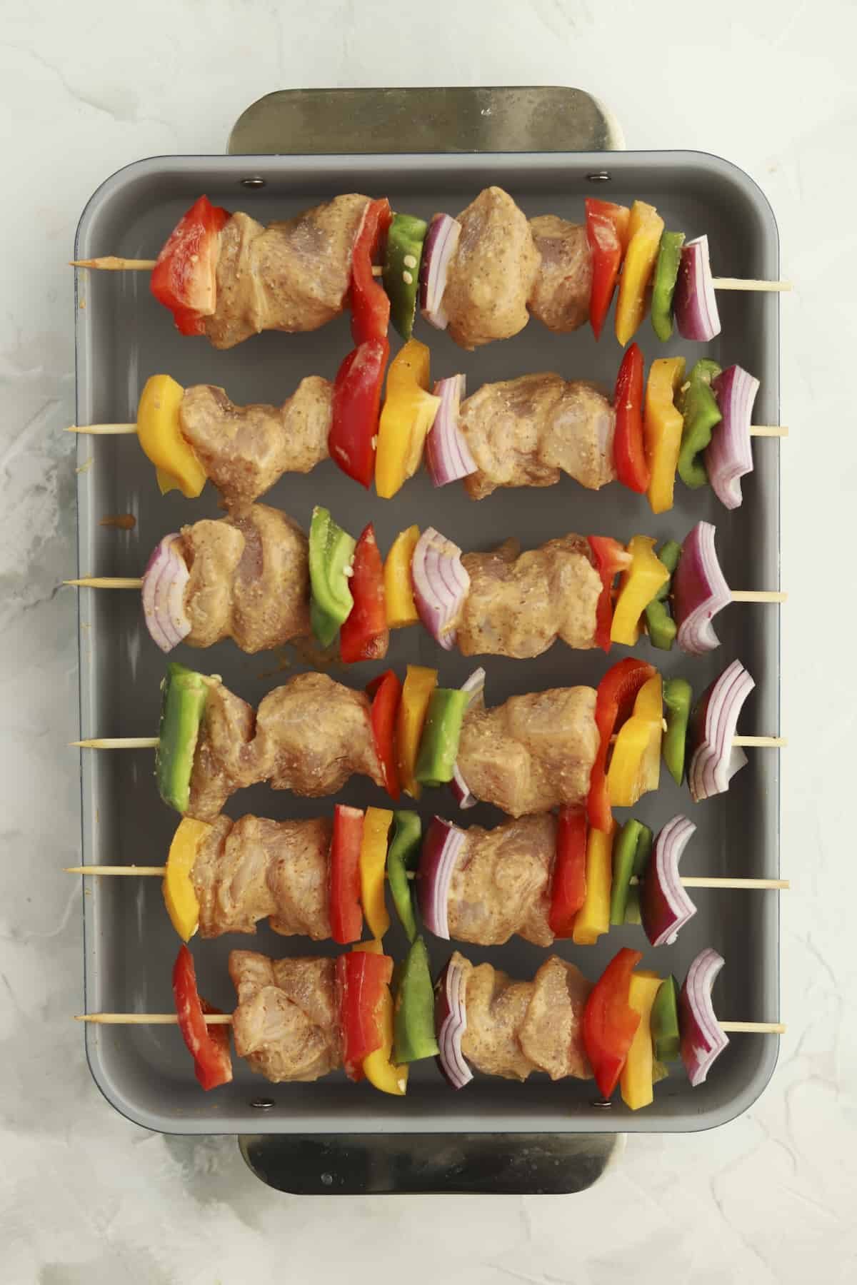 baking dish of raw chicken skewers with veggies