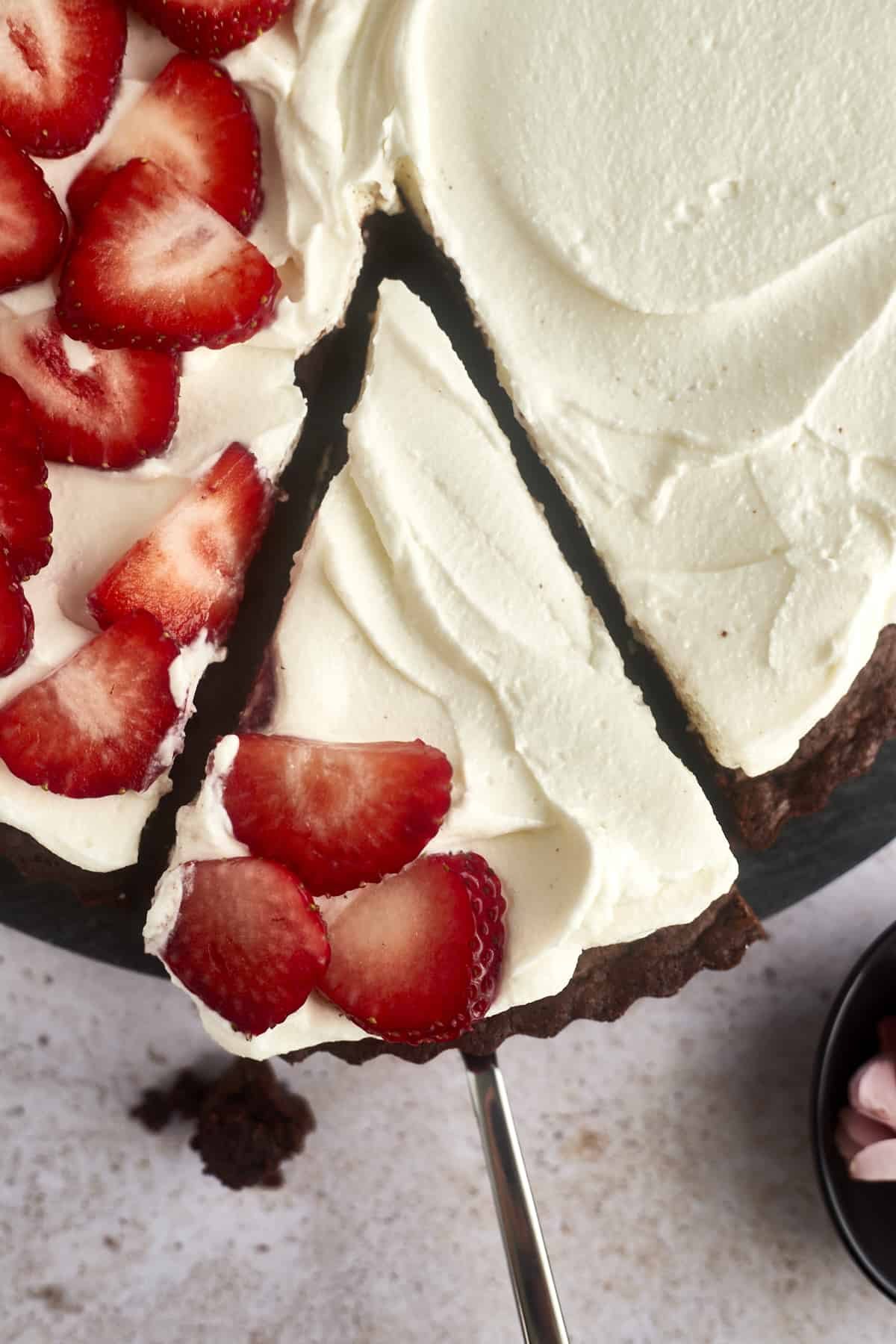 a sliced of brownie pizza topped with whipped cream frosting and strawberries being lifted from the entire dessert pizza