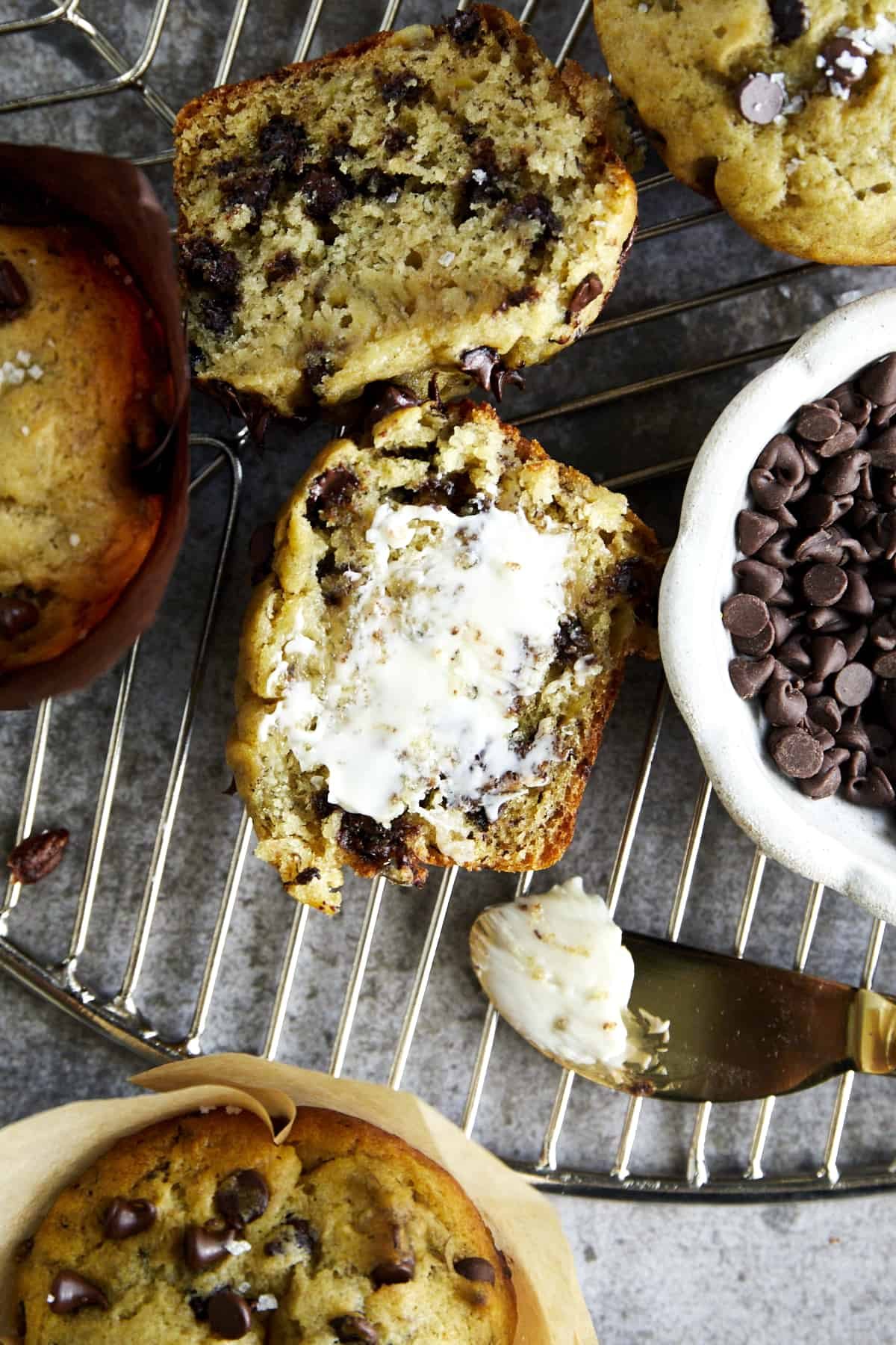A banana bread muffin with mini chocolate chips sliced in half with butter smeared on one side.