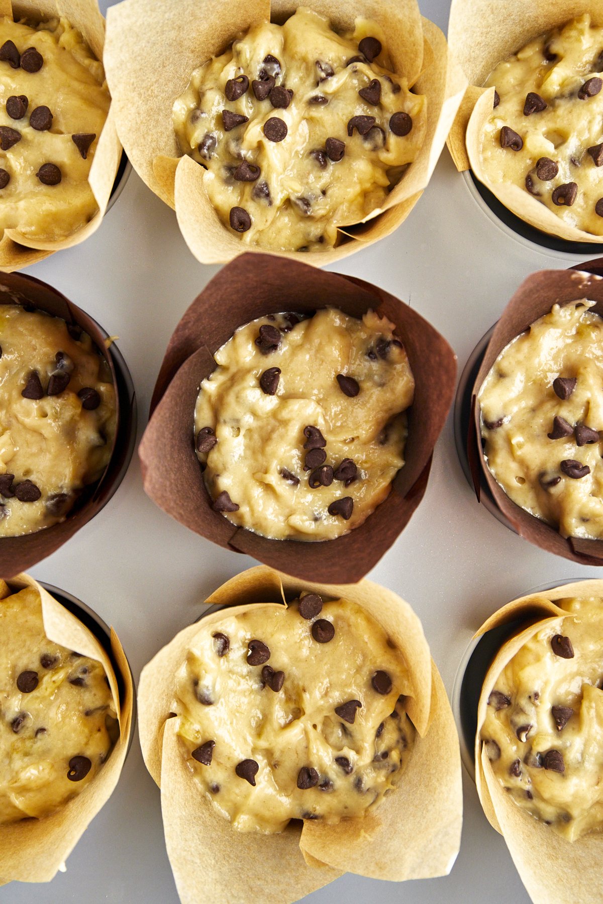 Unbaked banana bread muffins with chocolate chips in a muffin pan with paper liners.