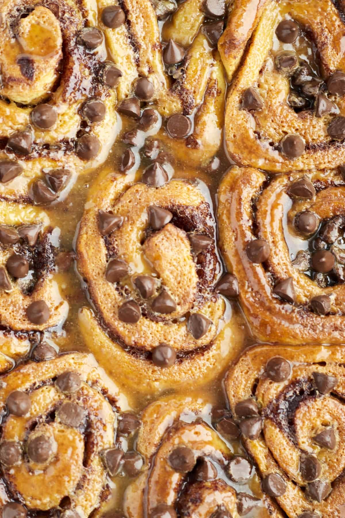 baked easy cinnamon rolls topped with caramel and chocolate chips in a white baking dish