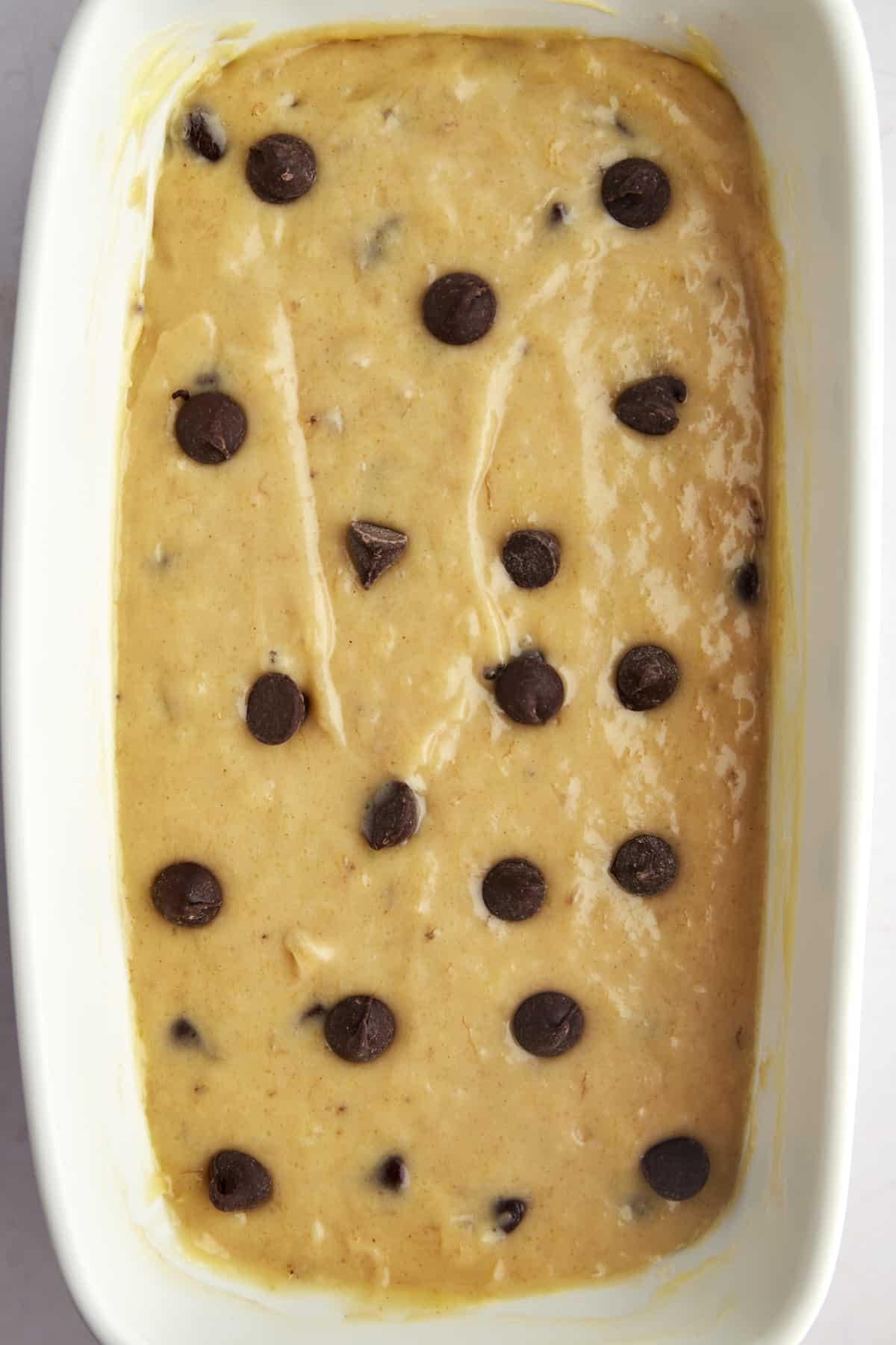 Overhead image of raw peanut butter banana bread batter topped with chocolate chips in a loaf pan.