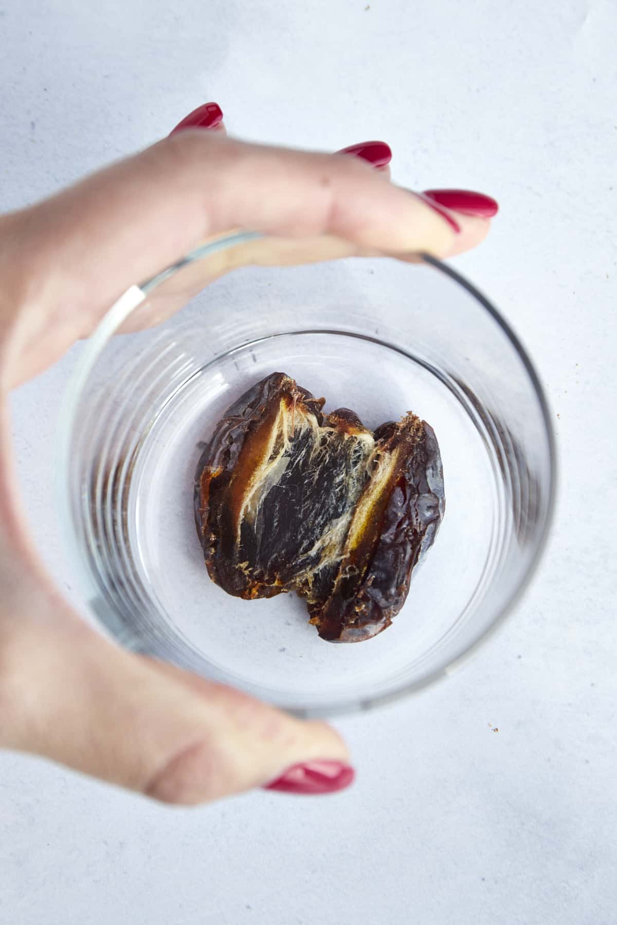 A hand using a cup to smash a date.